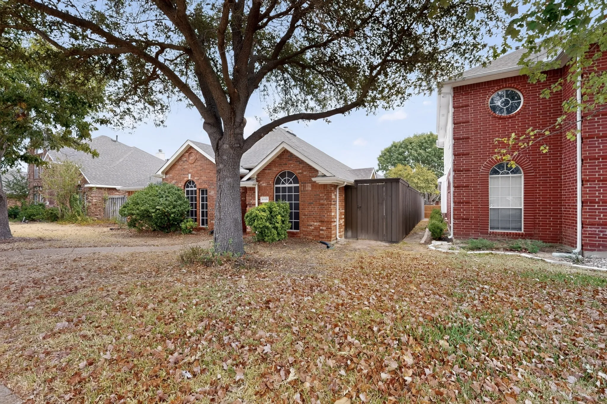 Brick exterior featuring arched windows, mature landscaping, and a side yard with privacy fencing