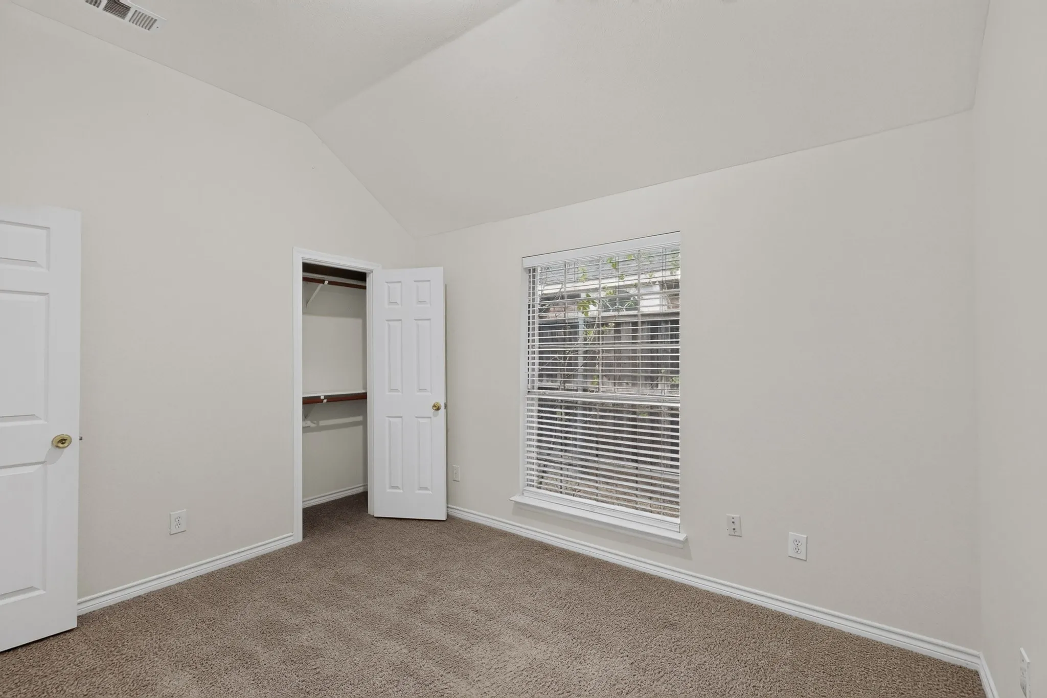 Vaulted ceiling, neutral wall paint, carpet flooring, a window with blinds, and built-in closet shelving