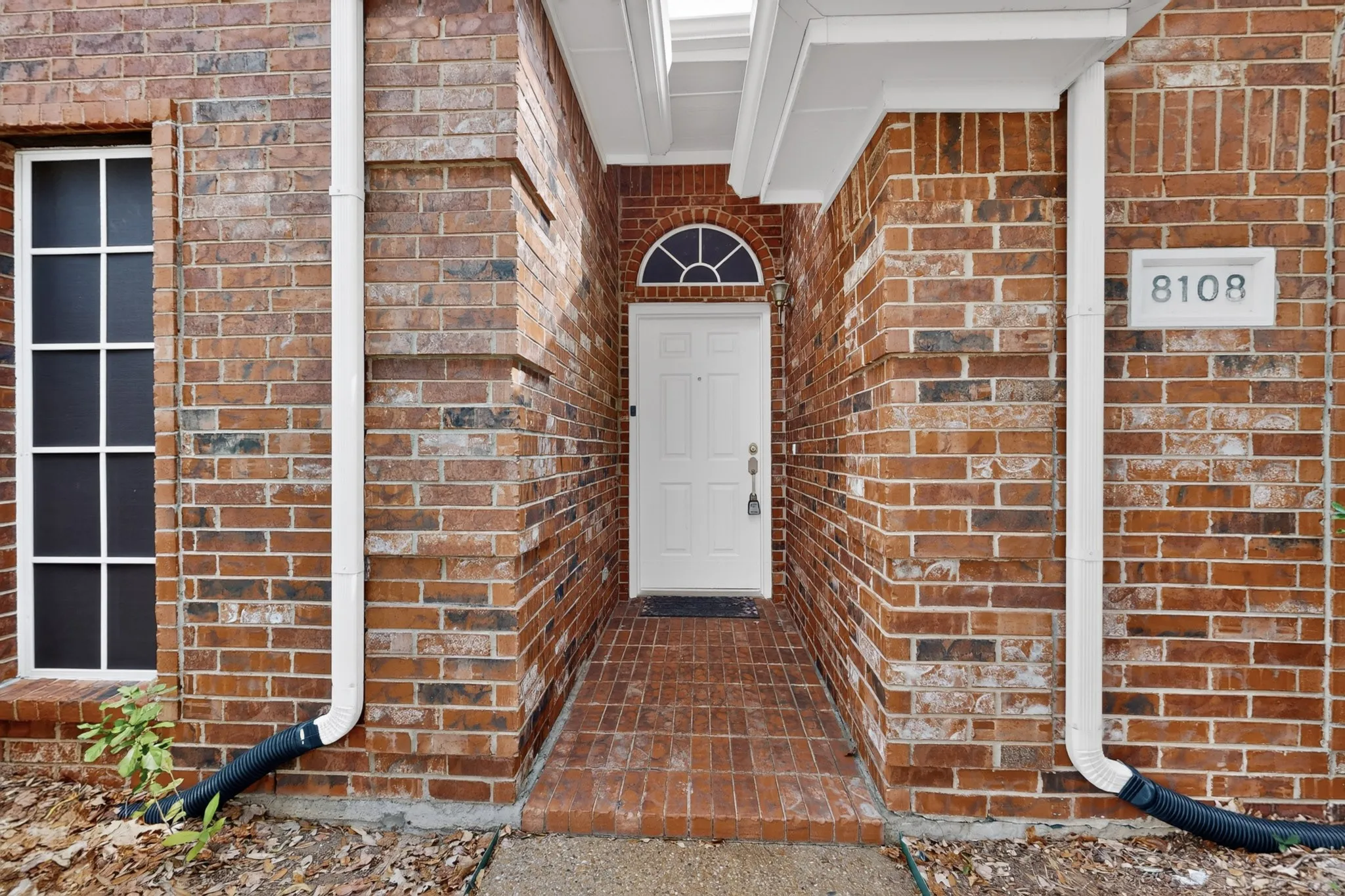 Brick exterior with white trim, arched window above the entry door, and a brick-paved entryway