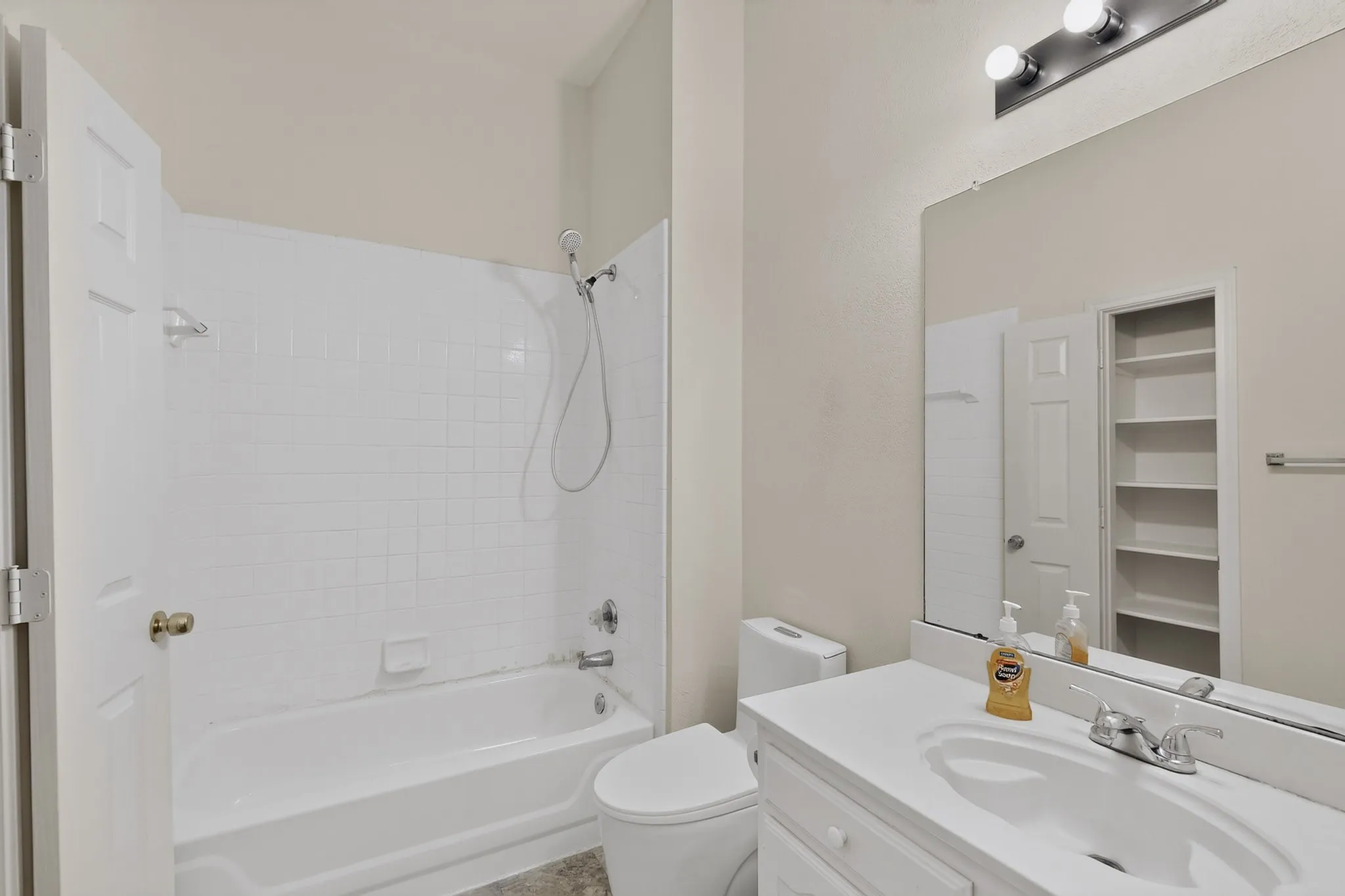 White tile shower surround, bathtub with shower fixture, single vanity with integrated sink, wall-mounted mirror, and built-in shelving