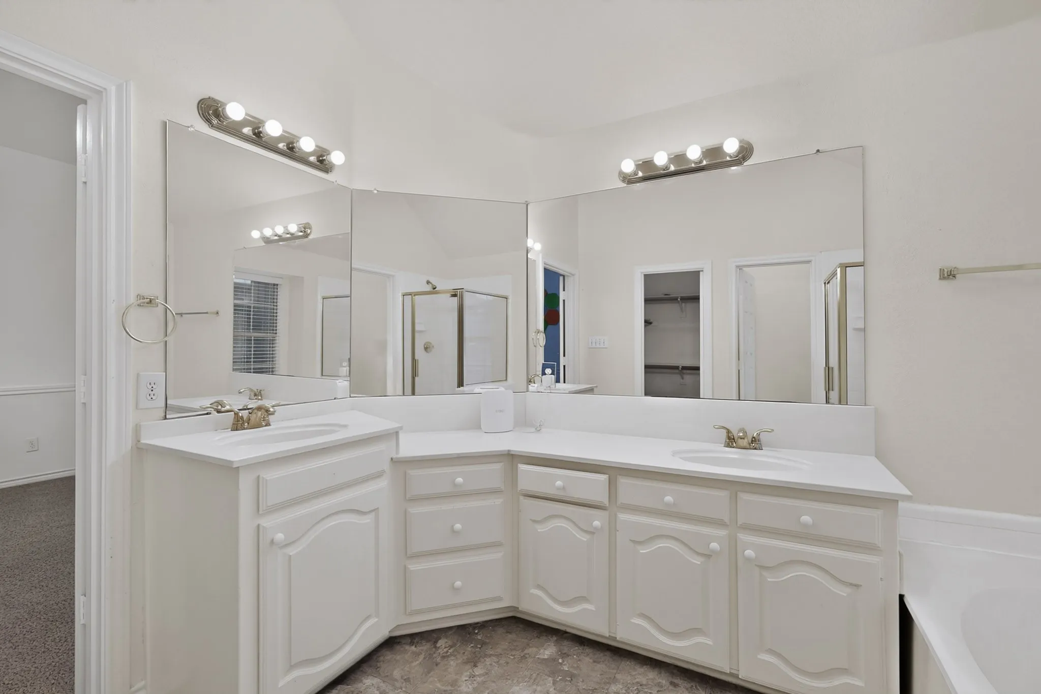 White cabinetry with integrated sinks, expansive wall-mounted mirrors, and an adjacent built-in soaking tub