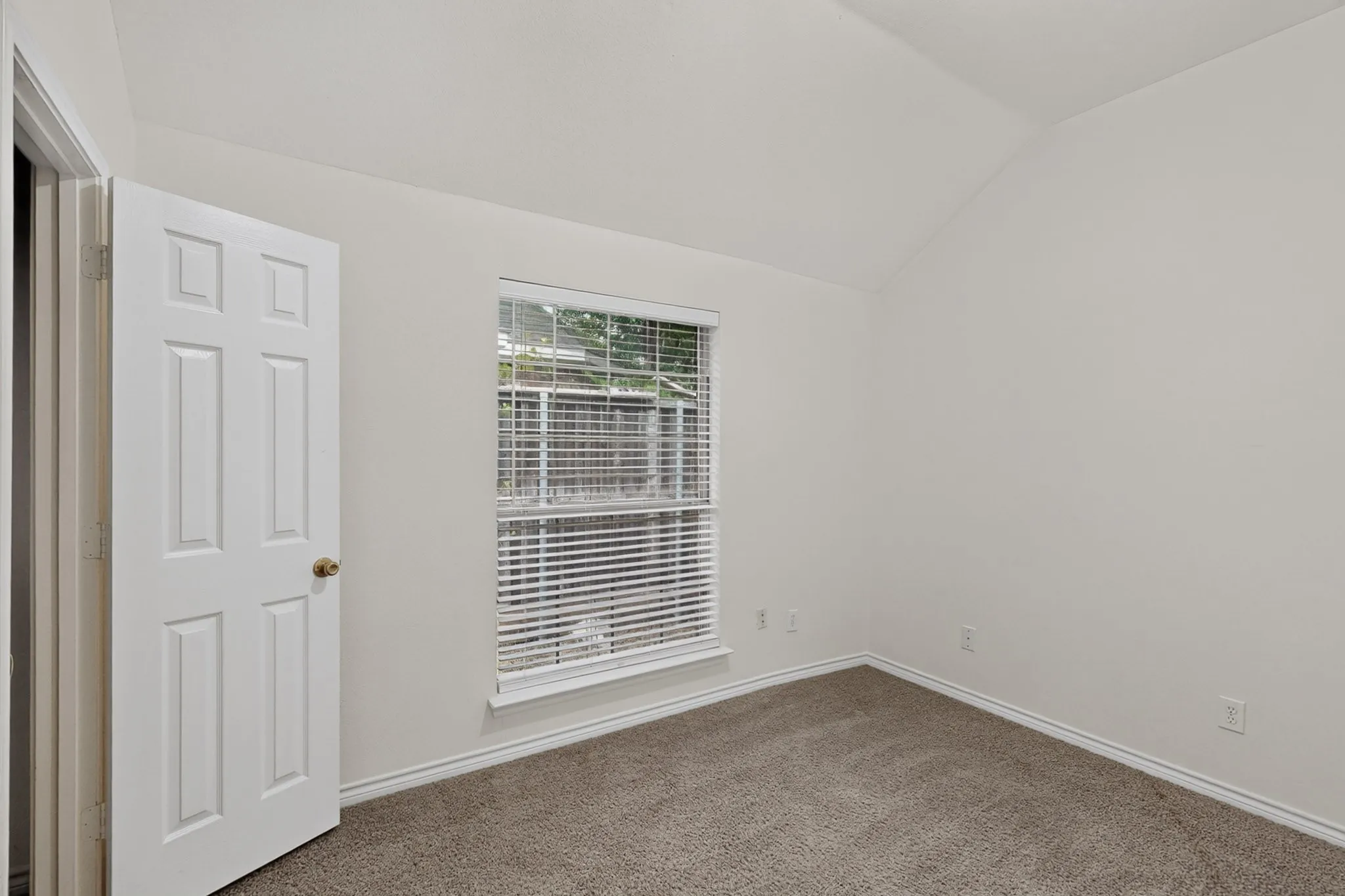 Angled ceiling, single window with blinds, six-panel interior door, wall-to-wall carpeting, and neutral wall tones