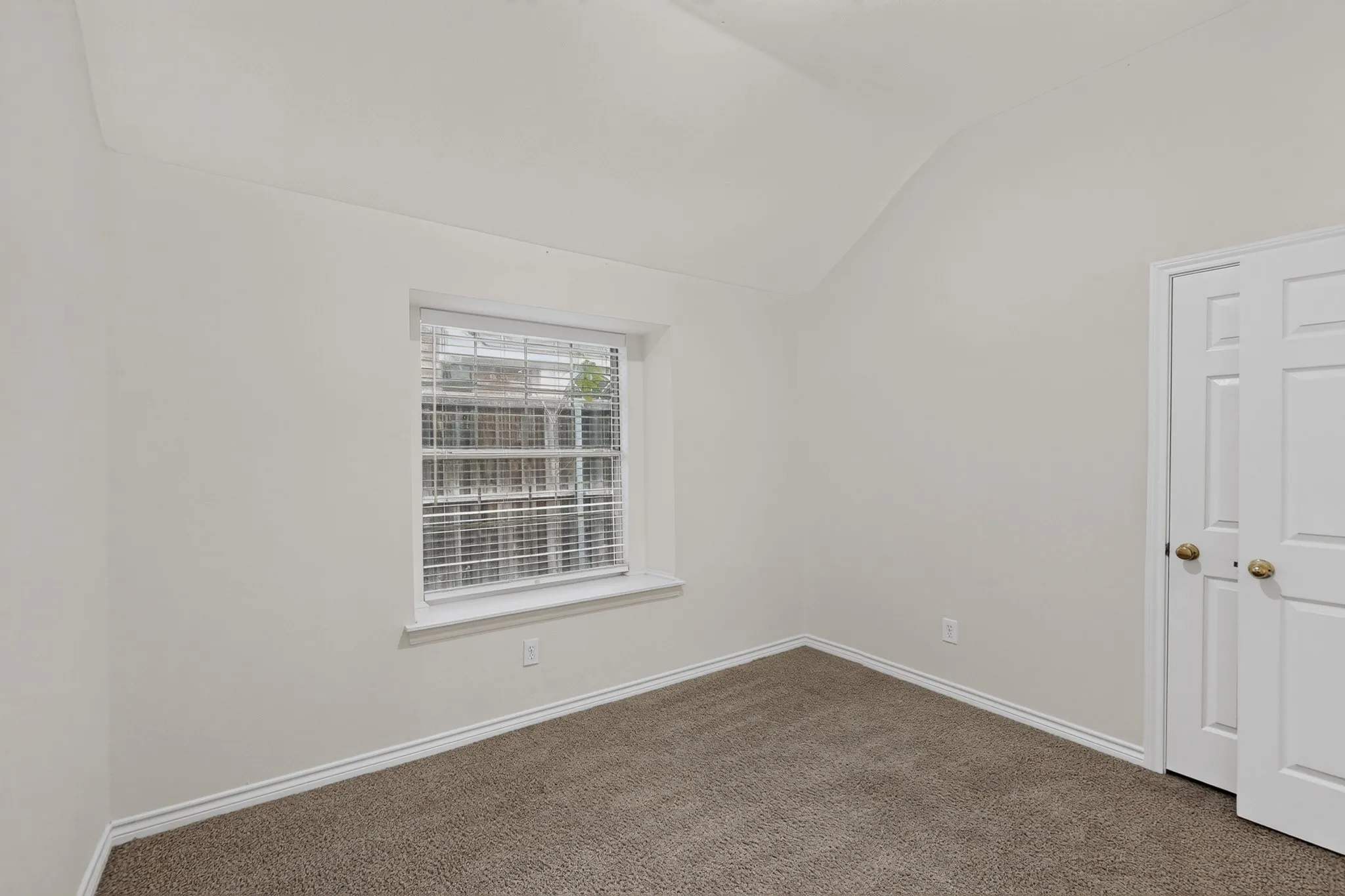 Vaulted ceiling, neutral wall paint, window with blinds, carpeted flooring, and a bifold closet door