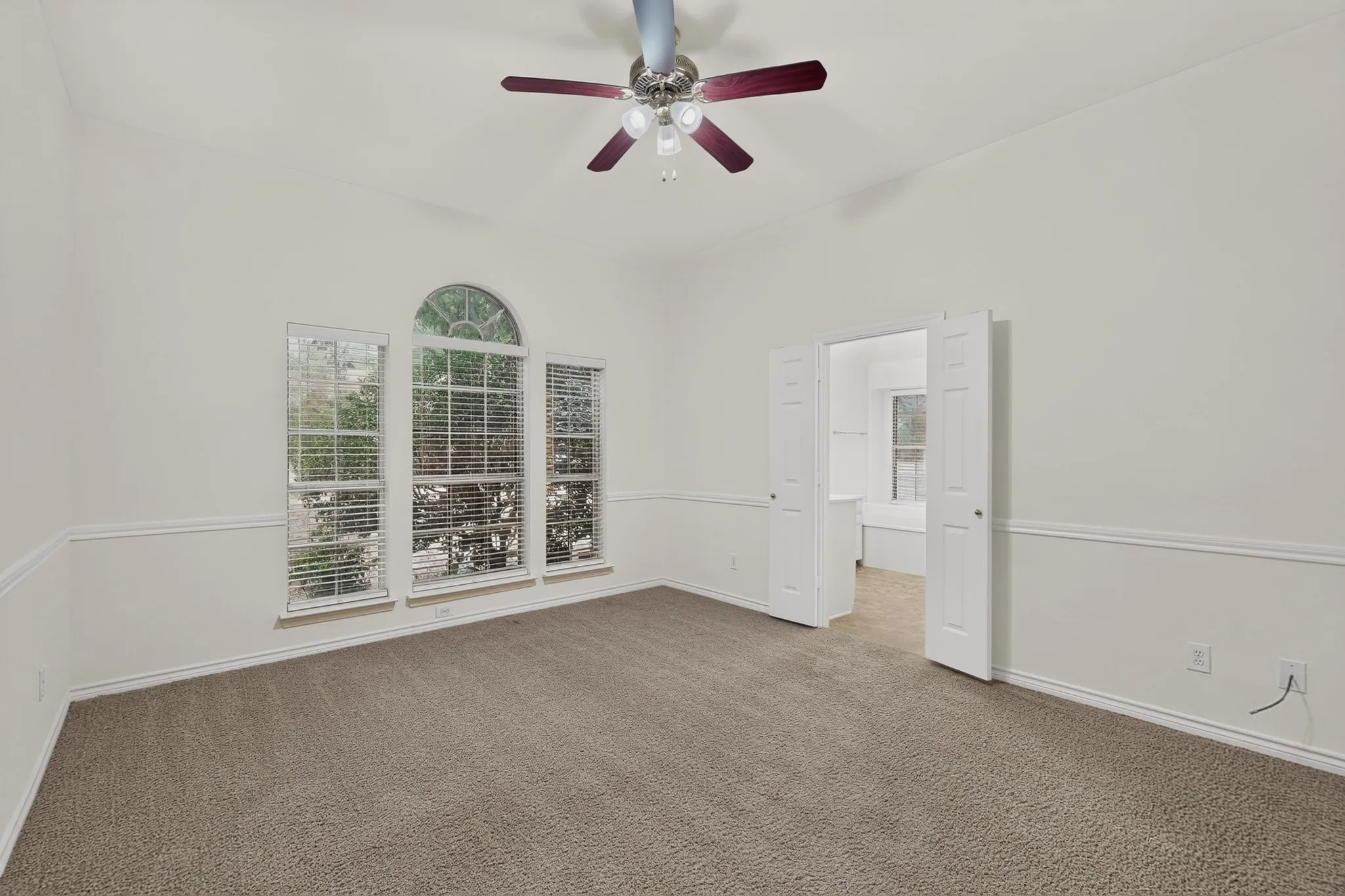 High ceilings, arched window accent, neutral carpet, bi-fold doors, and a ceiling fan