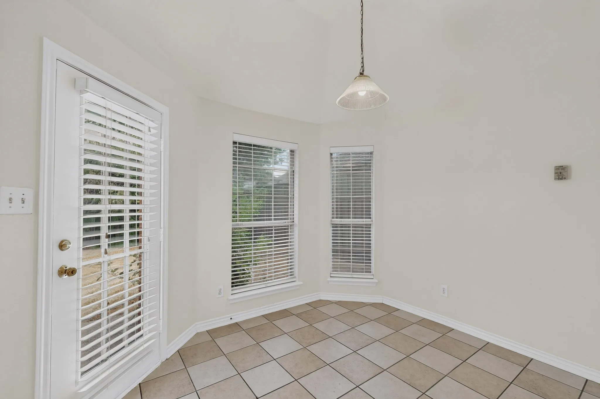 Vaulted ceiling with pendant lighting, ceramic tile flooring, multiple windows with blinds, and a glass-paneled door