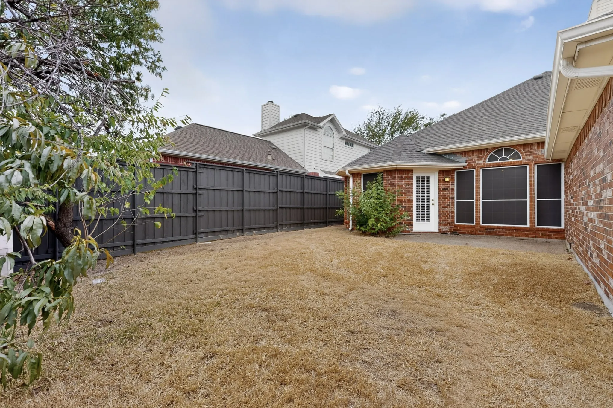 Private backyard featuring a dark wood fence and a brick exterior with a white door