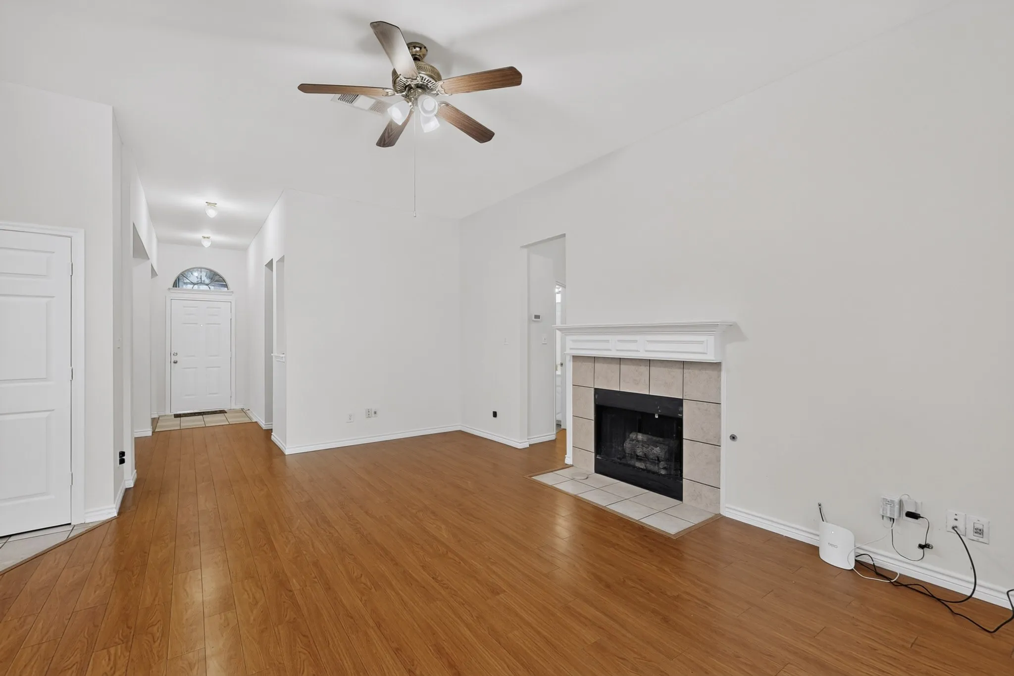 Vaulted ceiling with a ceiling fan, fireplace with a tile surround and mantel, wood-finish flooring, and an arched transom window above the entry door