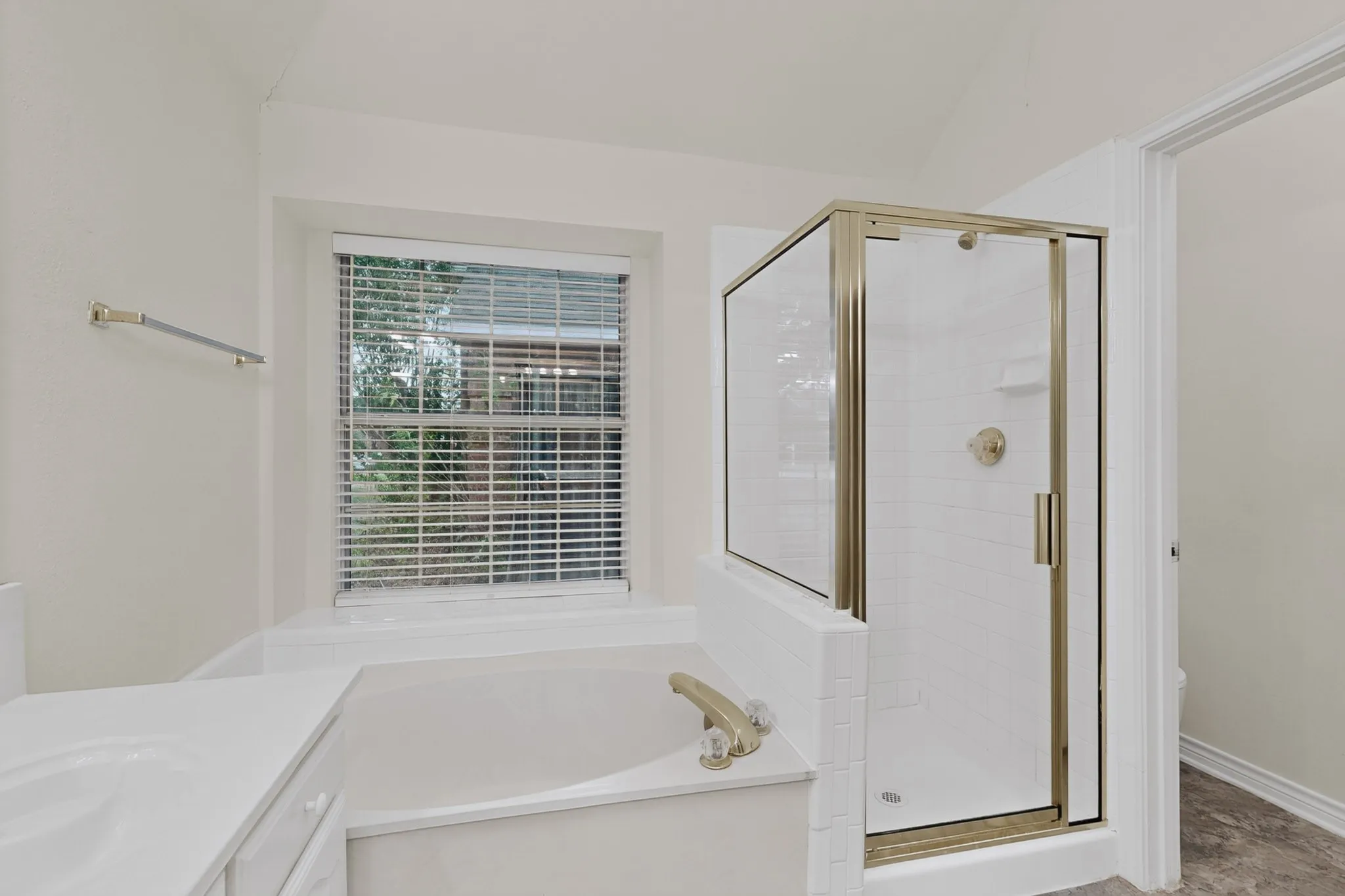 Built-in soaking tub with gold-tone fixtures, separate shower with glass enclosure, white tile surround, and a vanity with an integrated sink