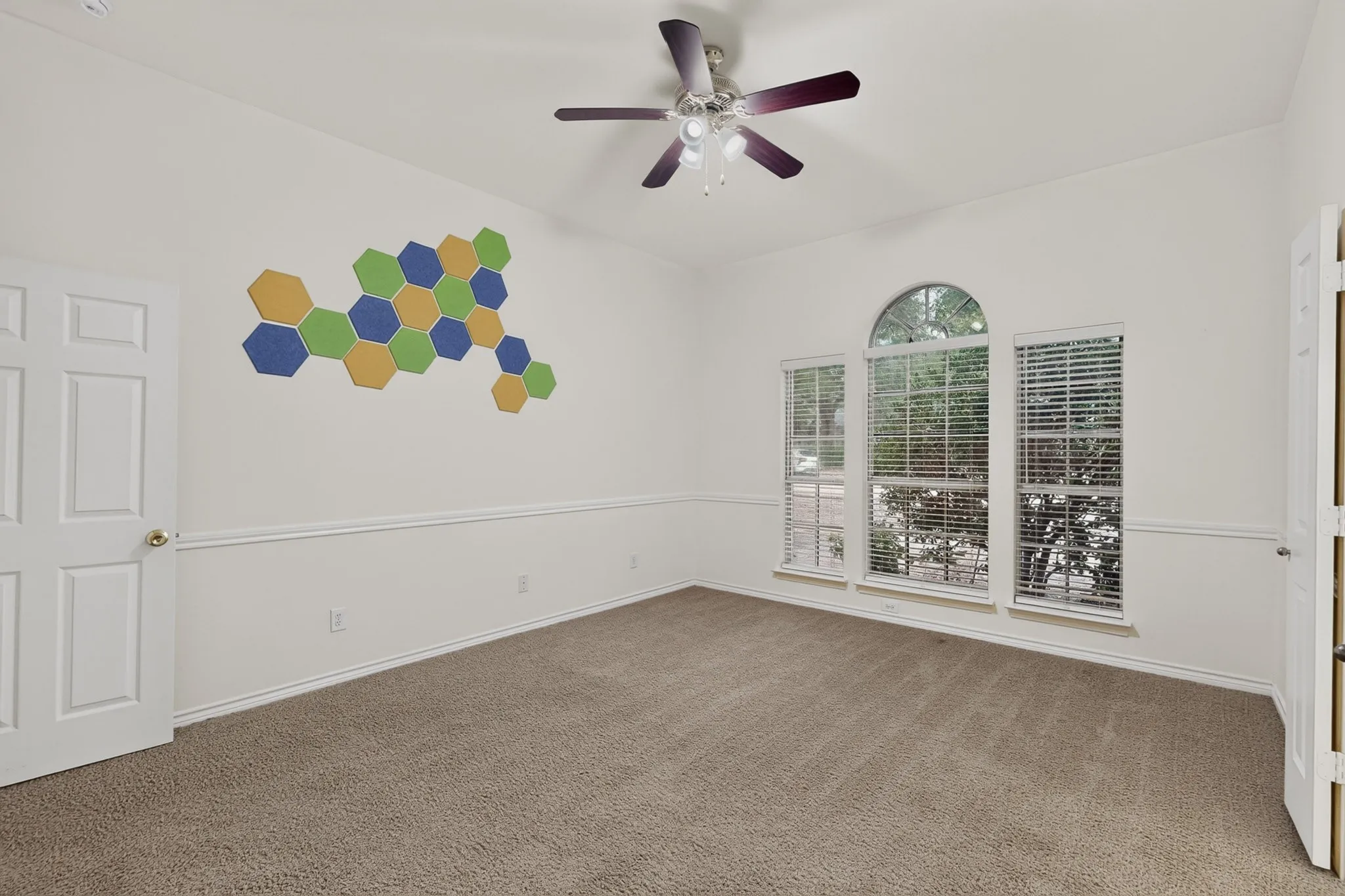 Arched window with two flanking windows, ceiling fan, and neutral carpet