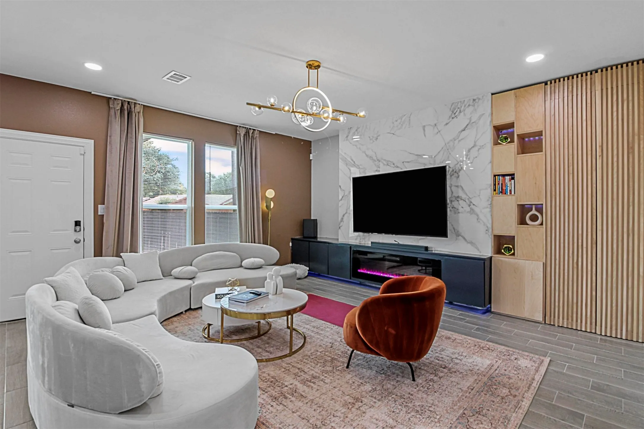 Recessed lighting, wood-finish flooring, built-in media console, marble-look accent wall, and a decorative ceiling fixture