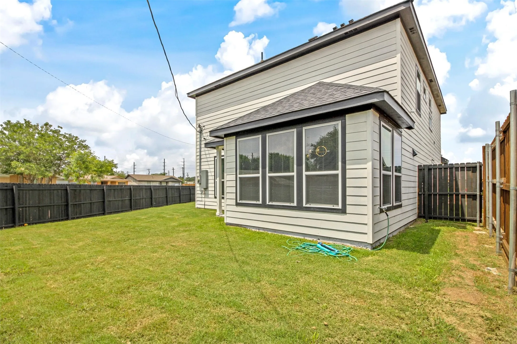 Expansive grassy yard with a dark wood fence and a bay window extension featuring multiple windows
