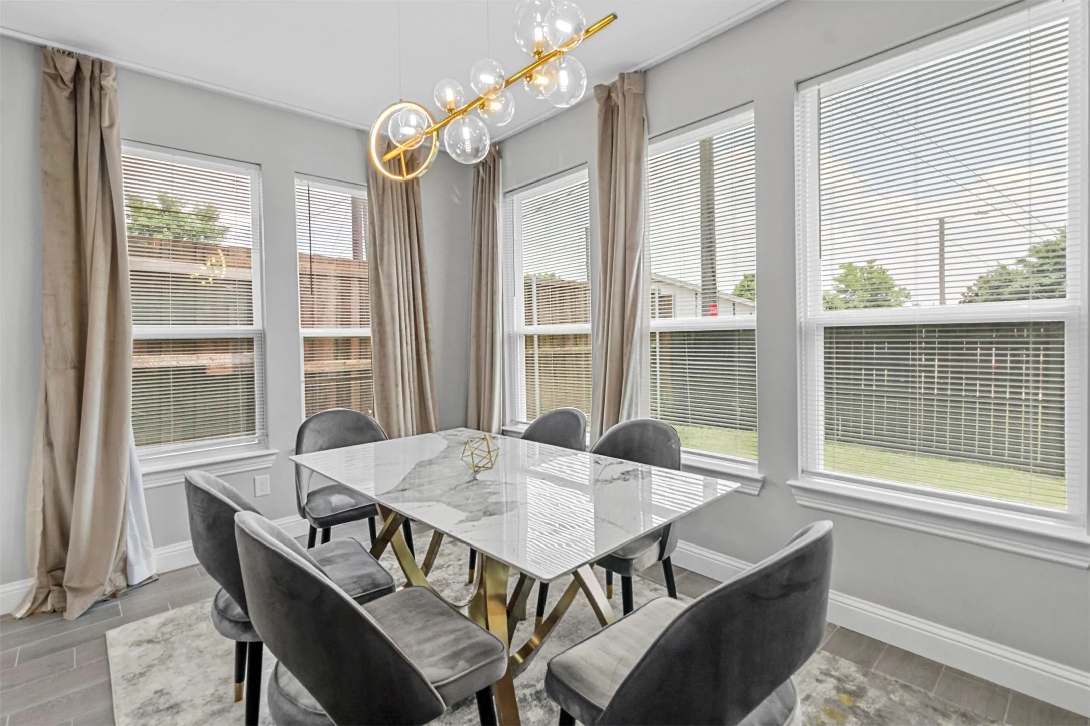 Multiple large windows with white frames, a contemporary chandelier, light gray wall paint, and tile flooring