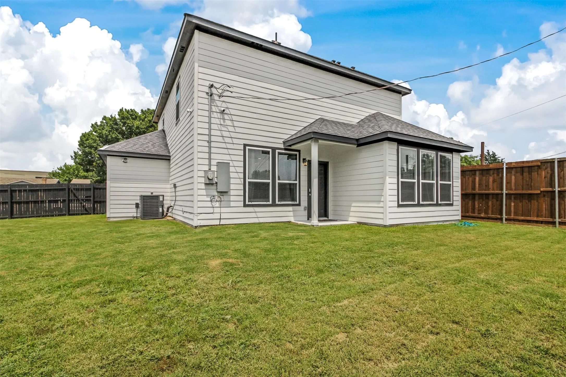 Expansive lawn area with a multi-pane window bay, covered patio, and privacy fencing