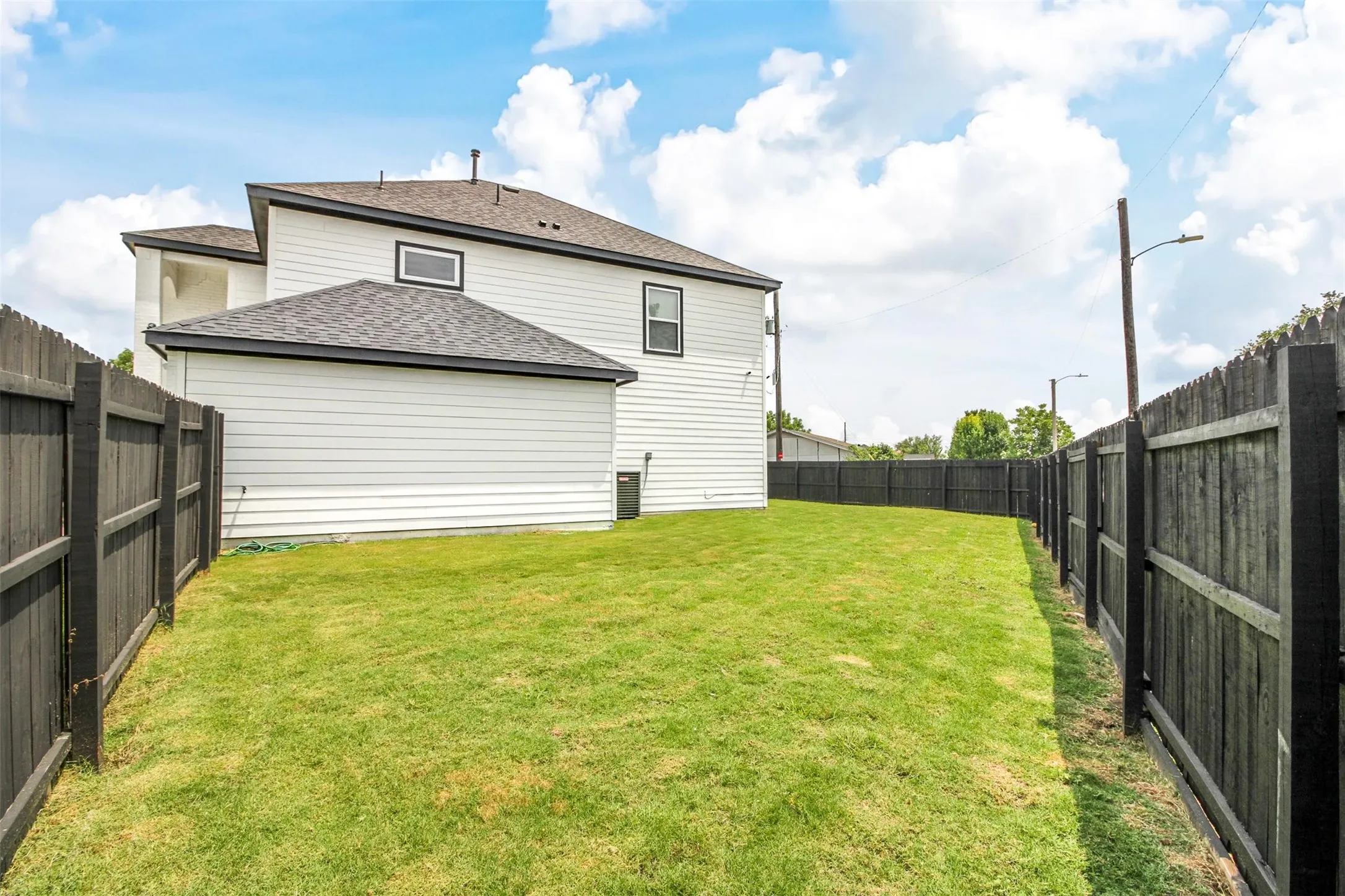 Expansive backyard featuring a manicured lawn, full perimeter privacy fencing, and two-story siding exterior with dark trim
