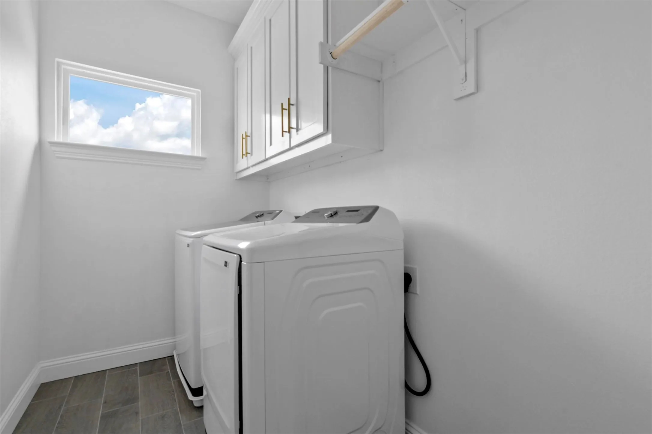 Laundry area featuring wood-finish flooring, white cabinetry with brass hardware, and a window for natural illumination