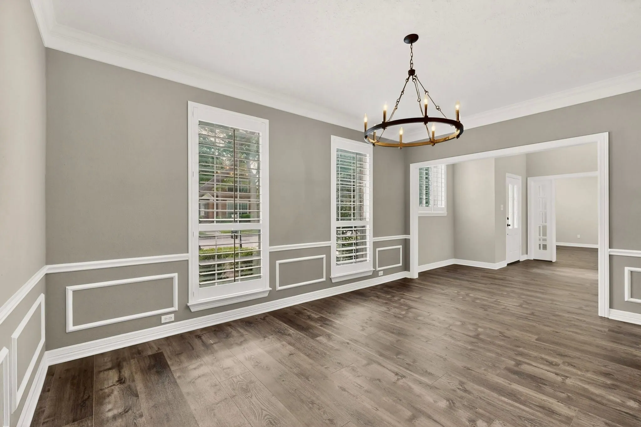 Decorative wainscoting with crown molding, wood-finish flooring, and a chandelier with a dark bronze finish