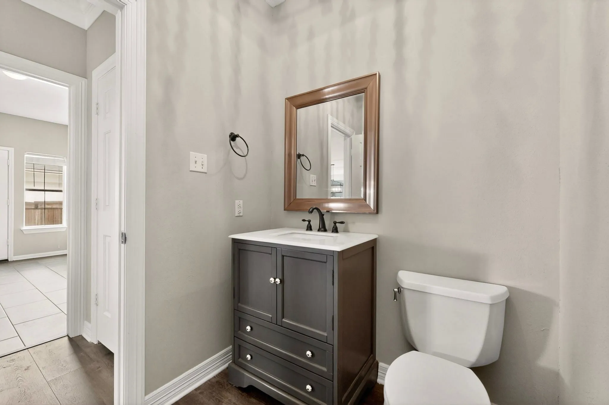 Powder room featuring a dark wood-finish vanity with a white countertop, a rectangular mirror with a wood frame, and wood-finish flooring