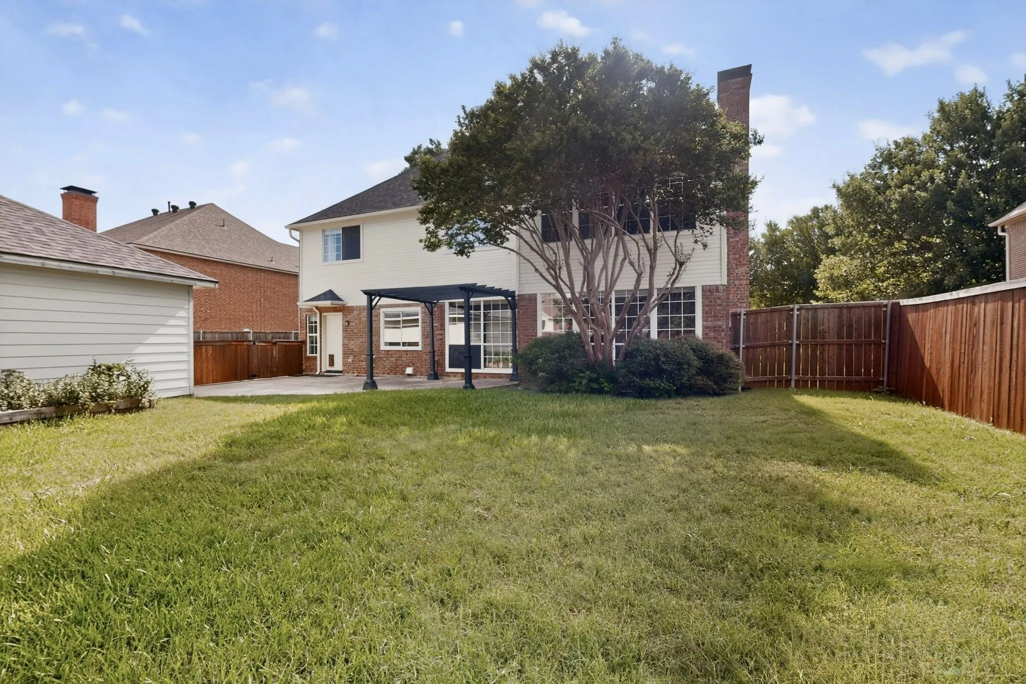 Expansive backyard featuring a concrete patio, a dark-toned pergola, and a privacy fence