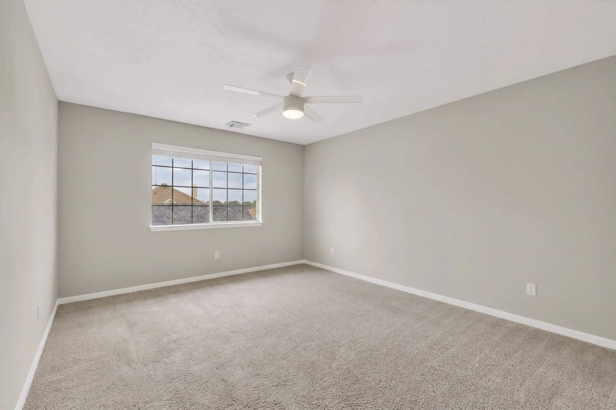 Spacious room with light-colored carpeting, a multi-pane window, and a ceiling fan with integrated lighting