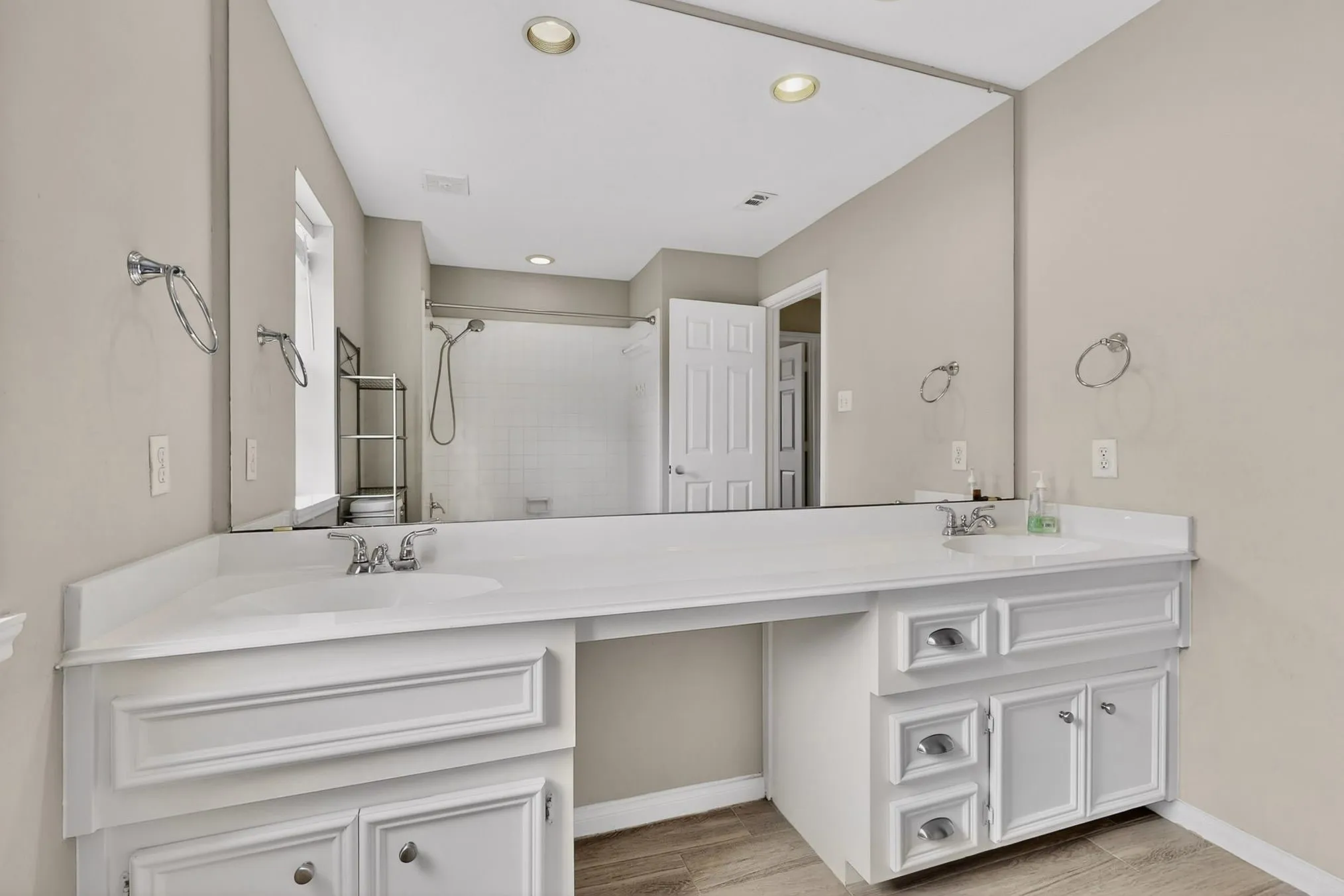 Dual vanity with white cabinetry, integrated sinks, chrome hardware, and a large wall-mounted mirror
