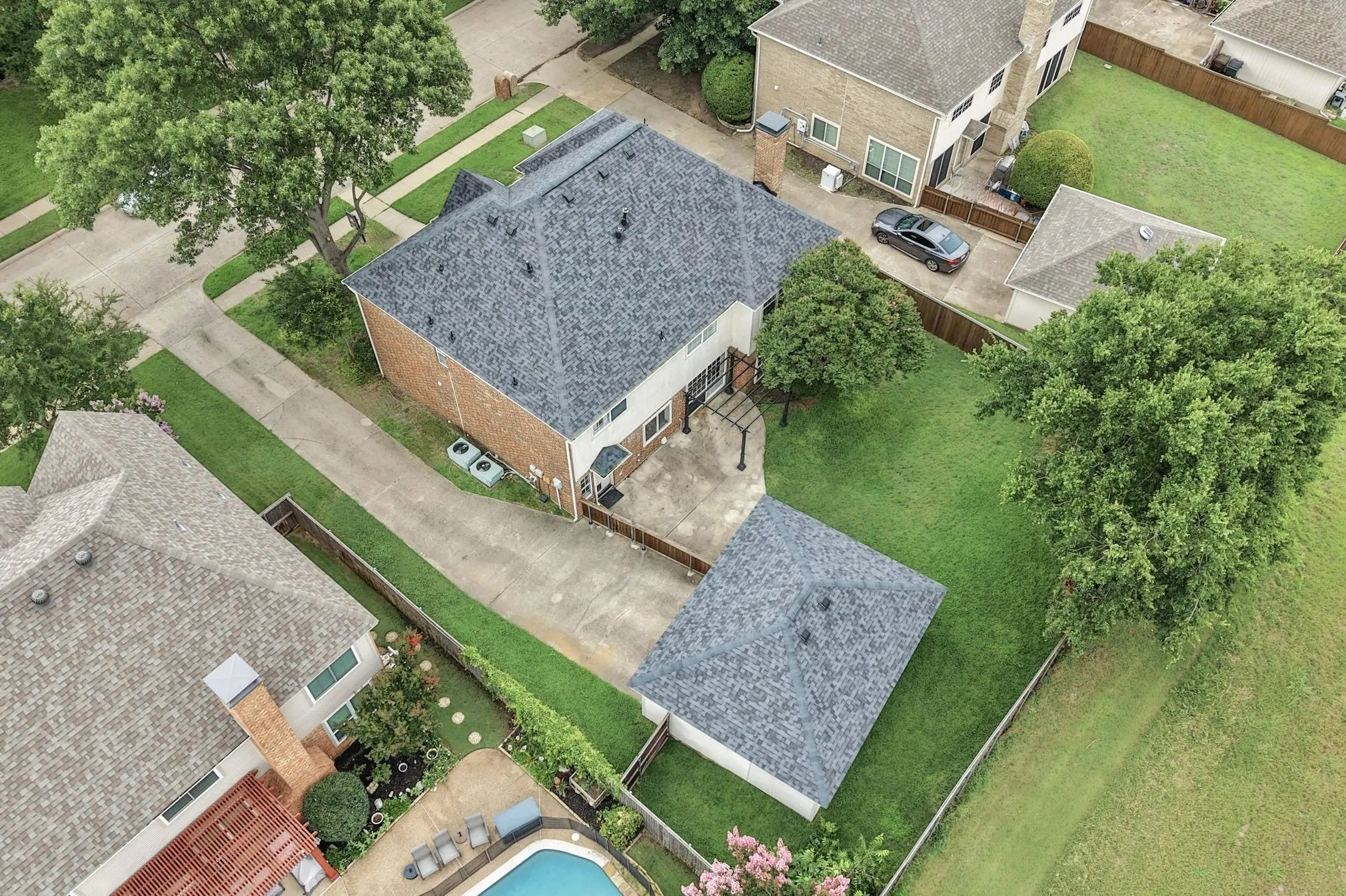 Expansive backyard featuring a manicured lawn, mature shade trees, and a detached structure with a shingle roof