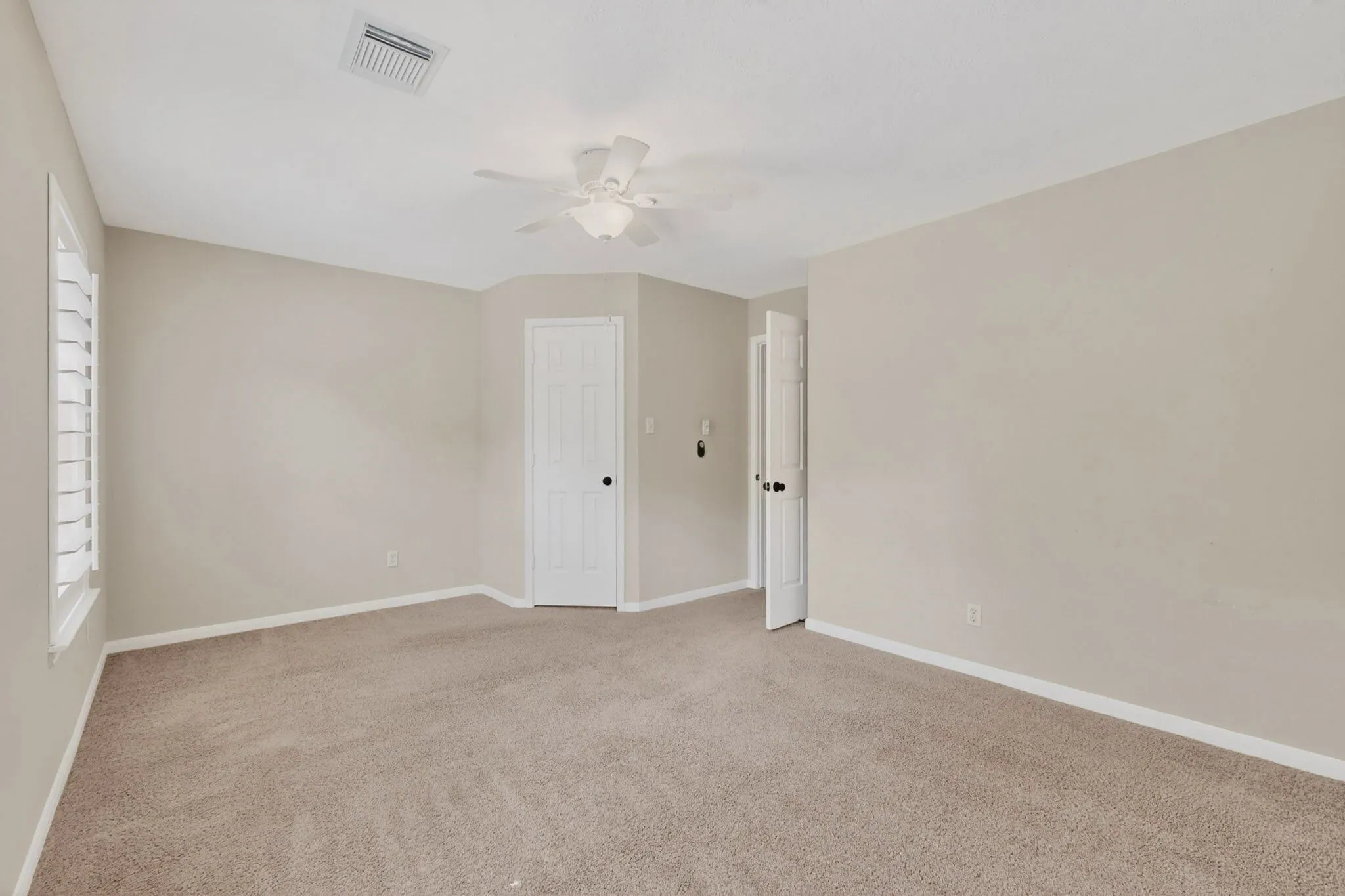 Plush carpet flooring, neutral paint tones, recessed ceiling fan, white interior doors, and window with plantation shutters