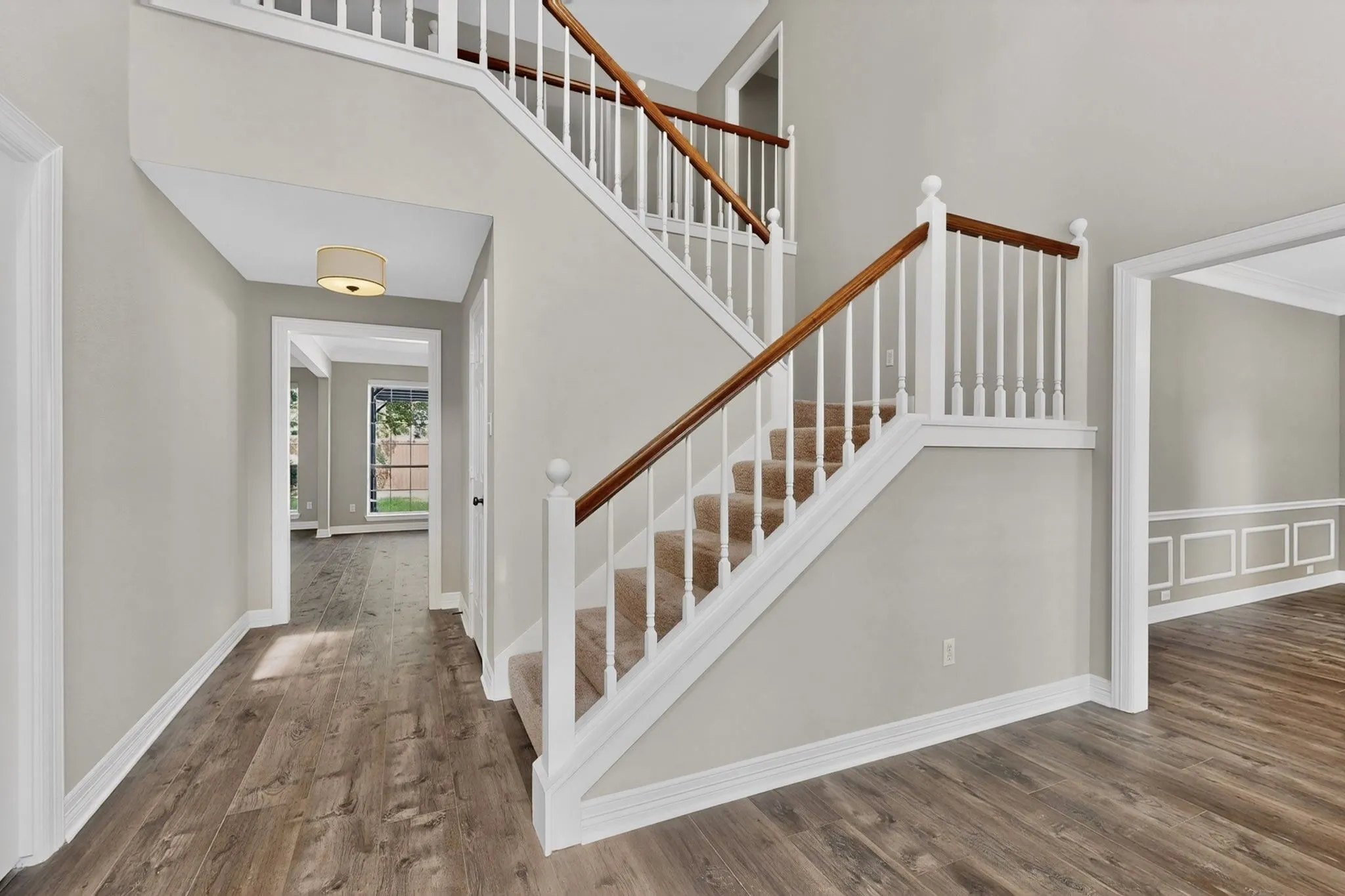 Staircase with carpeted treads and wood-finish handrails, wood-finish flooring, cased entryway, and wainscoting
