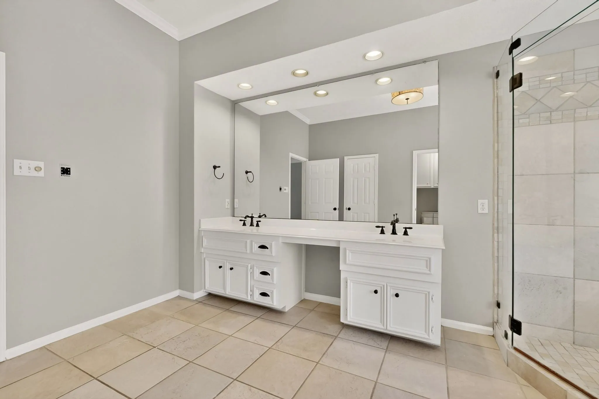 Dual vanity with white cabinetry and dark hardware, large wall-mounted mirror, recessed lighting, and a glass-enclosed shower with tile surround
