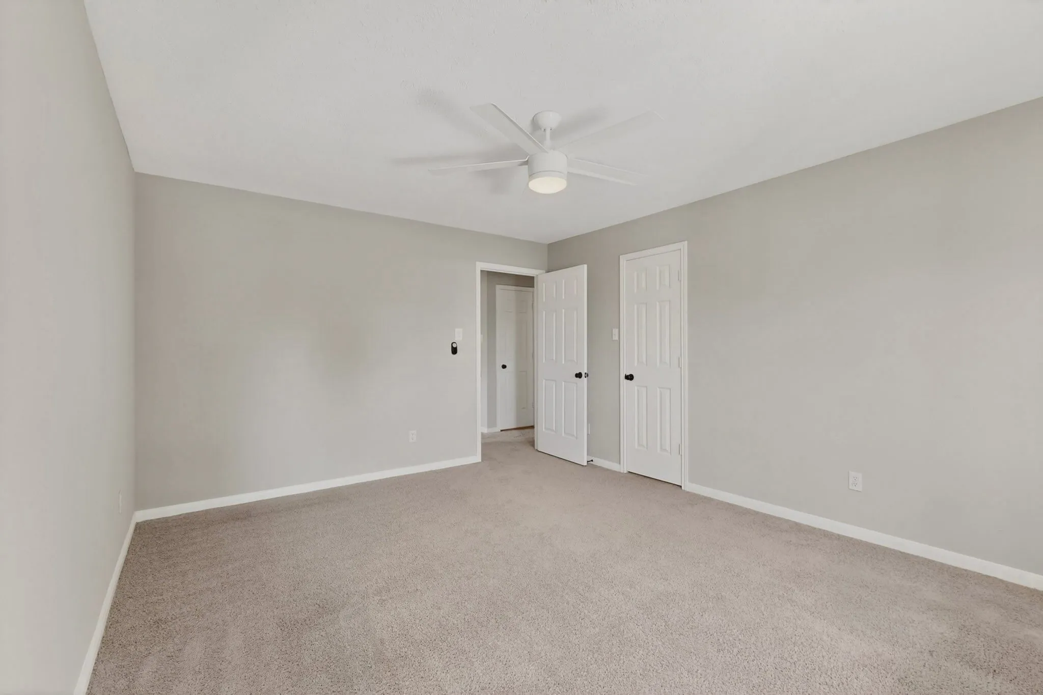 Neutral-toned walls, carpet flooring, a ceiling fan with integrated lighting, and white paneled doors