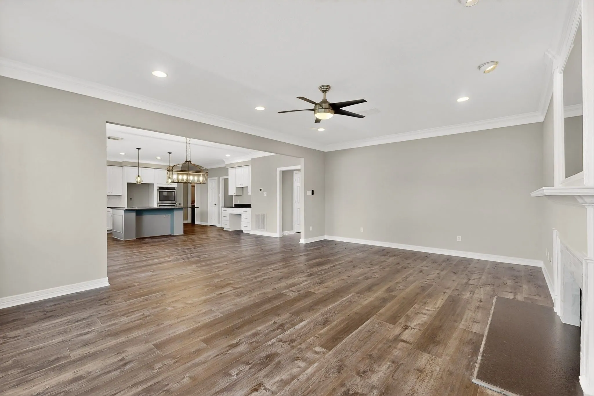 Wood-finish flooring, recessed lighting, crown molding, ceiling fan, and a built-in fireplace mantel