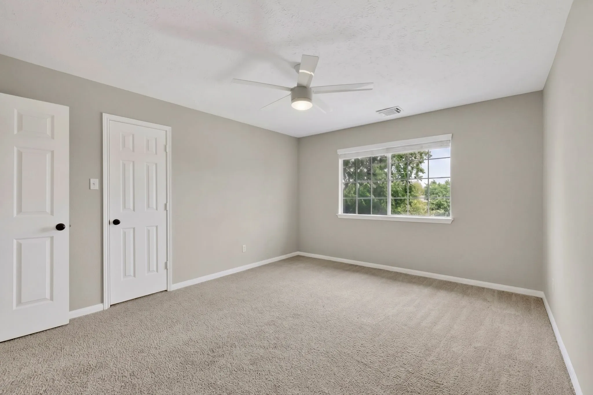 Neutral wall tones, carpet flooring, a ceiling fan with integrated lighting, and a single window