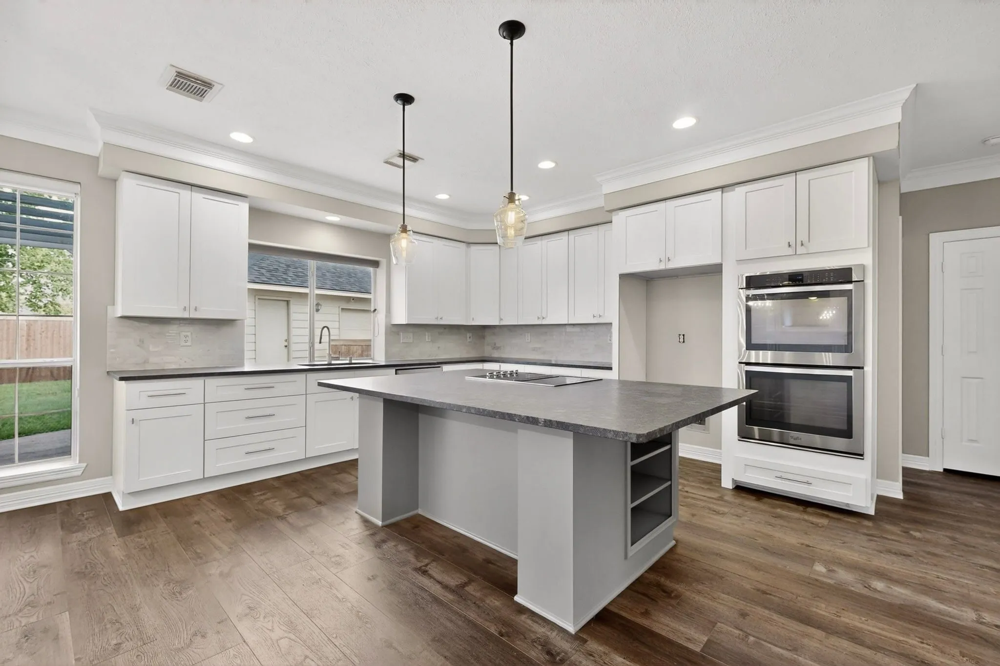 Spacious kitchen featuring white cabinetry, wood-finish flooring, a central island with integrated shelving, stainless steel double ovens, and recessed lighting