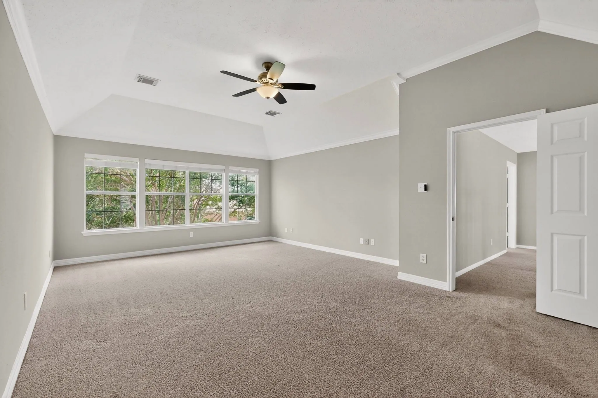 Spacious room featuring vaulted ceilings, a ceiling fan with integrated lighting, expansive windows with white trim, and neutral-toned carpeting