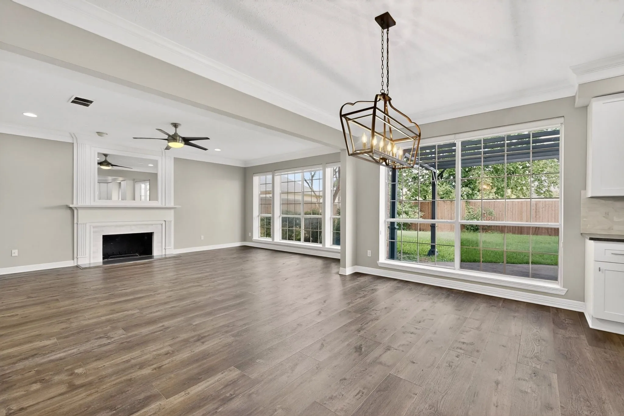 Spacious room with wood-finish flooring, a white mantel fireplace, and a ceiling fan