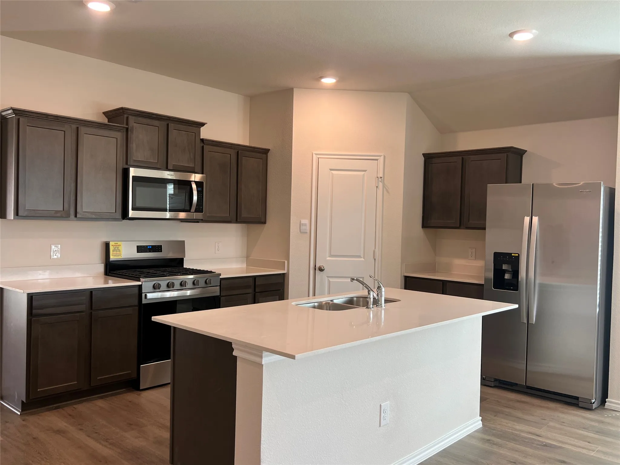 Kitchen featuring appliances with stainless steel finishes, dark brown cabinets, dark wood-style floors, recessed lighting, and a center island with sink