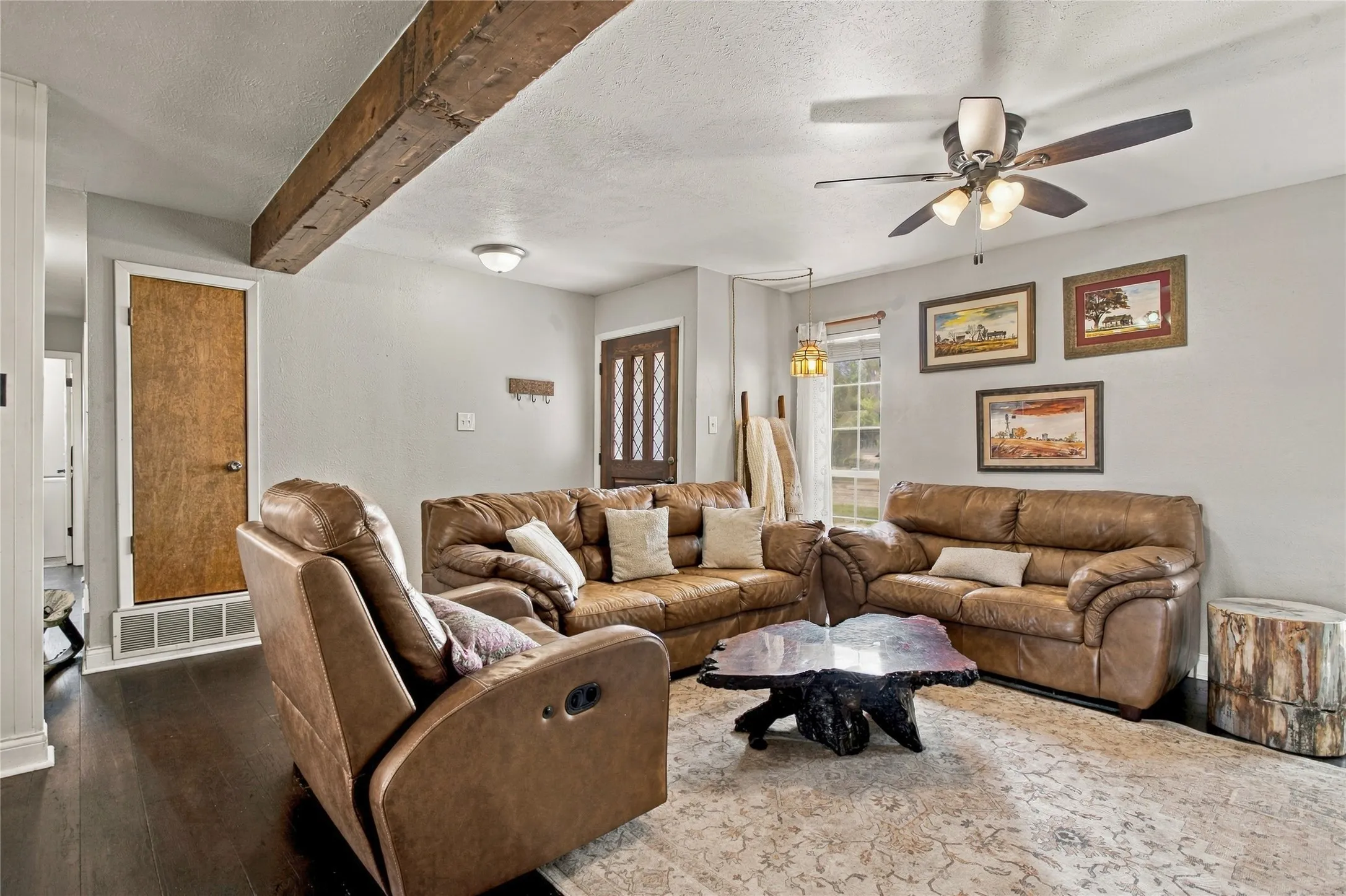 Wood-finish flooring, exposed ceiling beam, ceiling fan with integrated lighting, wood paneled door, and a built-in wall sconce