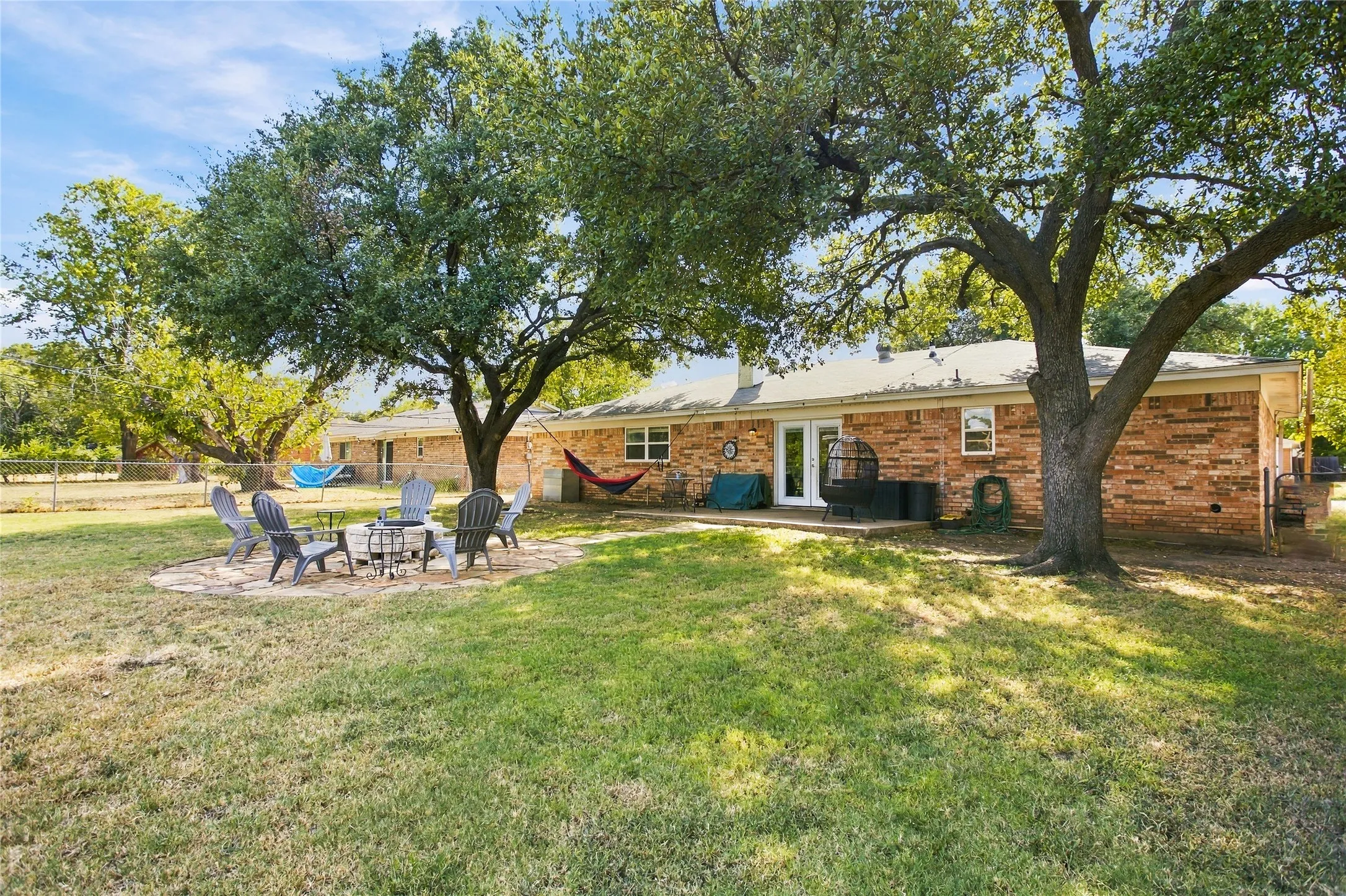 Expansive backyard featuring a manicured lawn, mature trees, and a flagstone patio with a built-in fire pit
