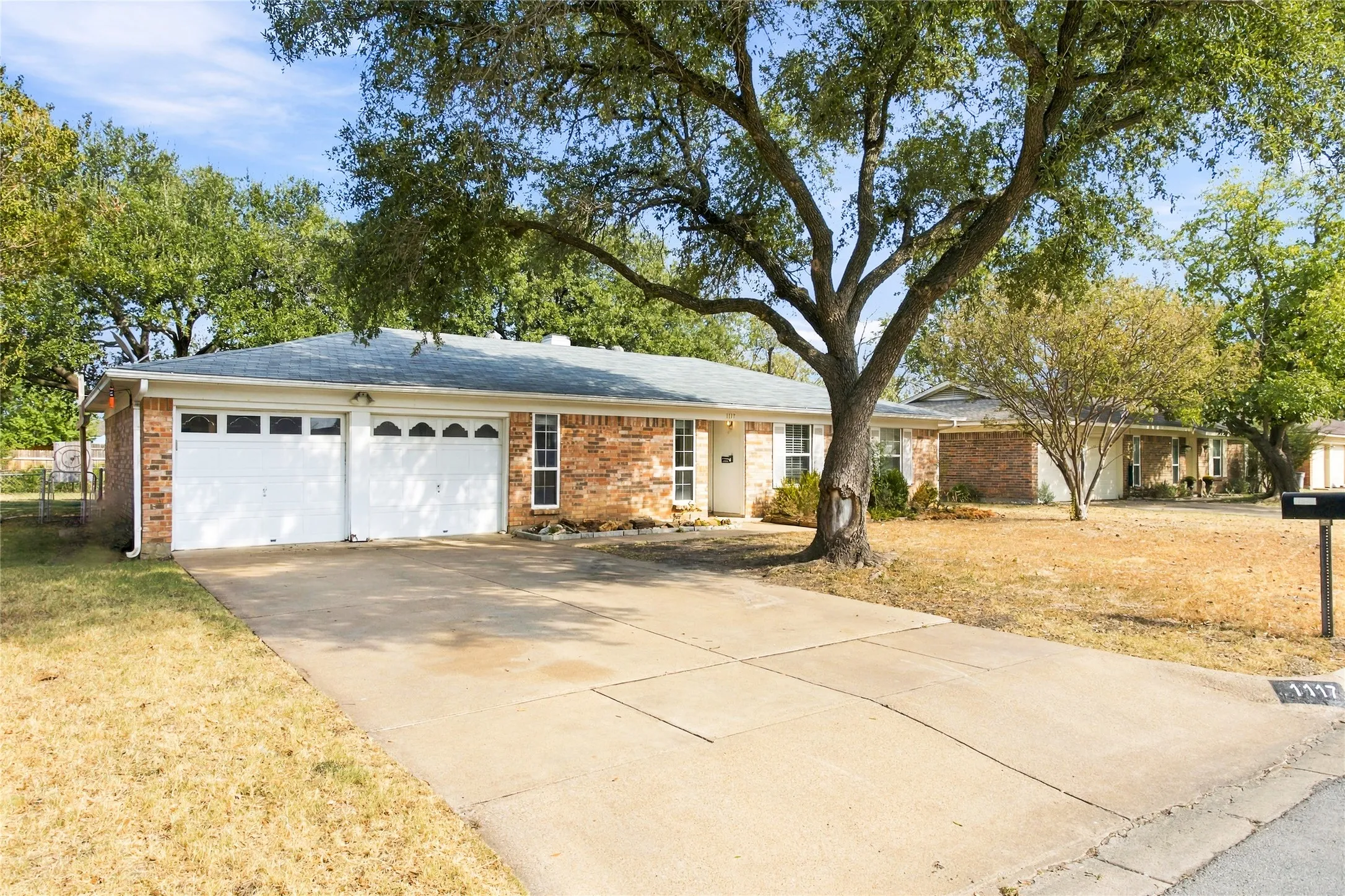 Brick facade residence with a two-car garage, concrete driveway, and mature trees