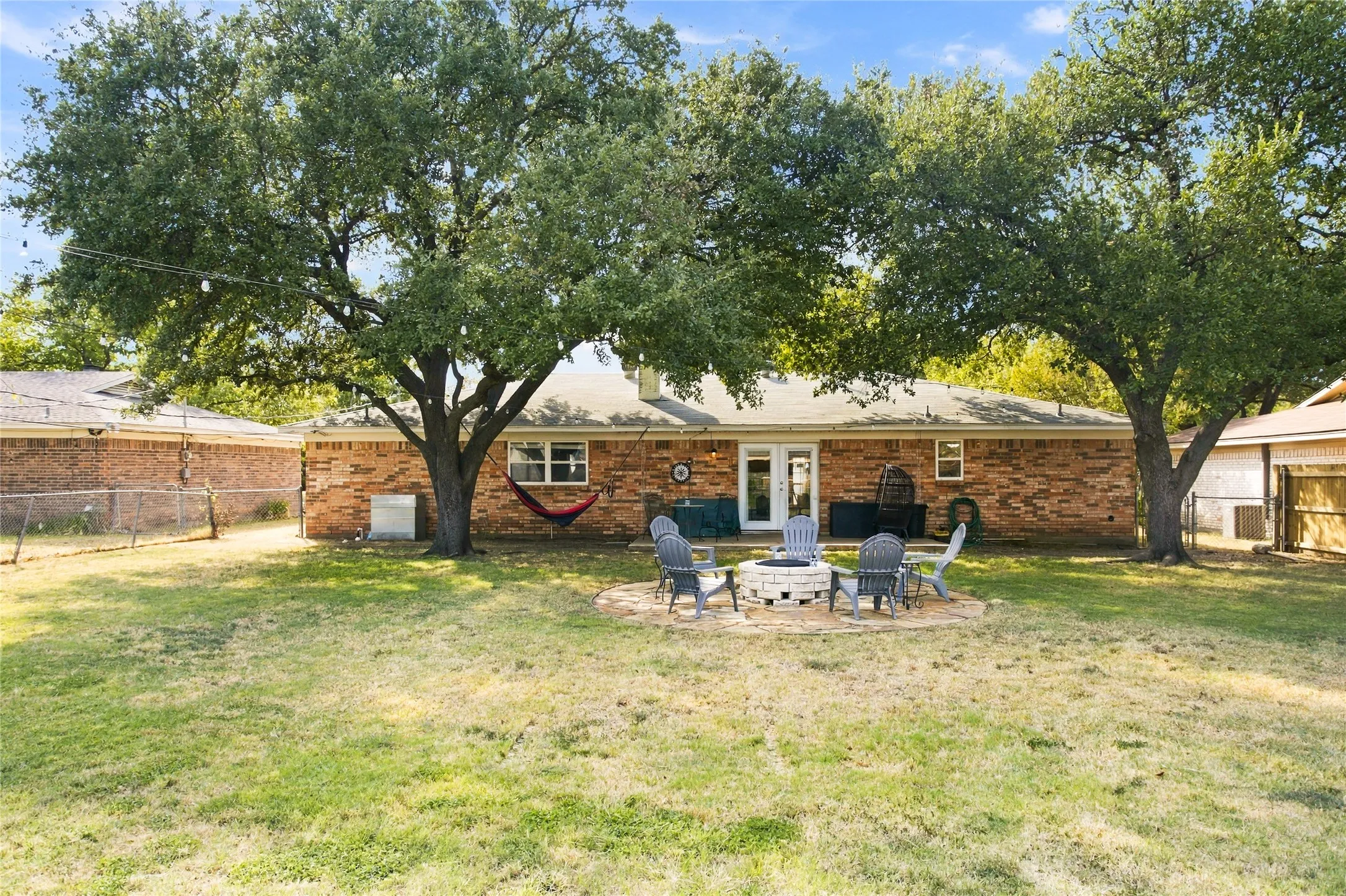 Expansive backyard featuring mature trees, a full brick exterior, a stone-paved fire pit area, and a rear patio