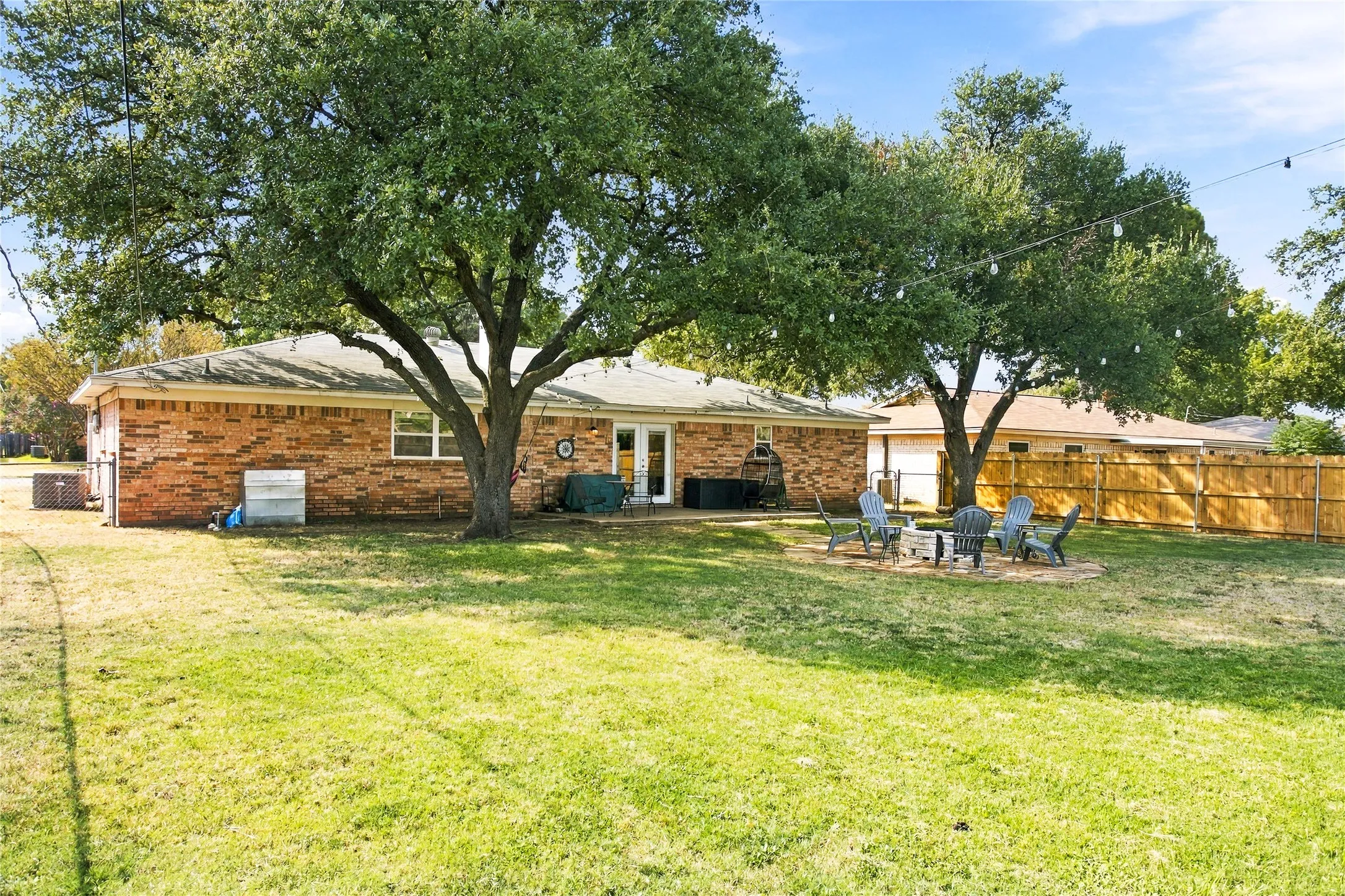 Expansive backyard with a brick-clad exterior, mature trees, and a wooden privacy fence