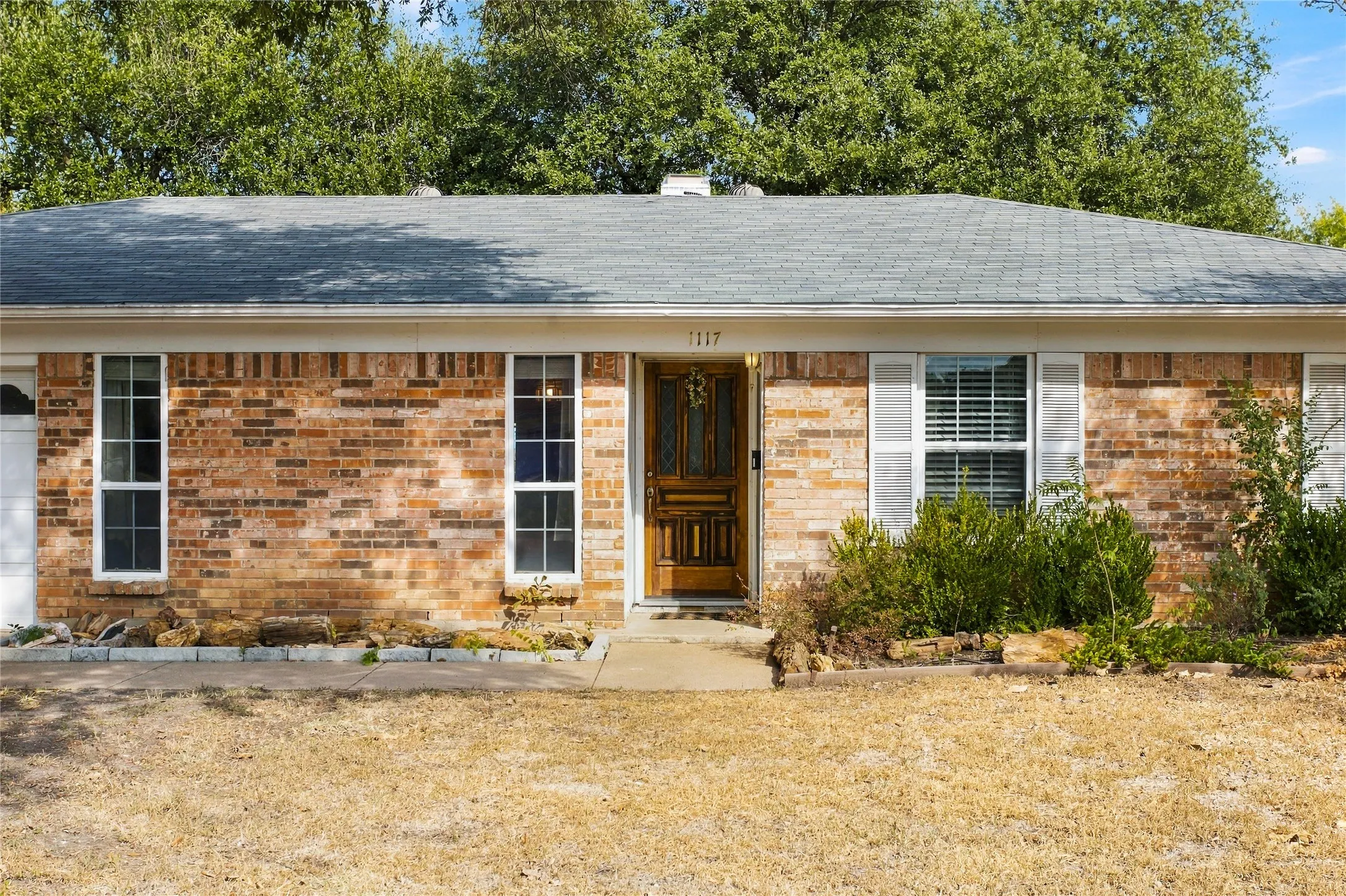 Brick exterior with a gray shingle roof, white trim, and a paneled front door