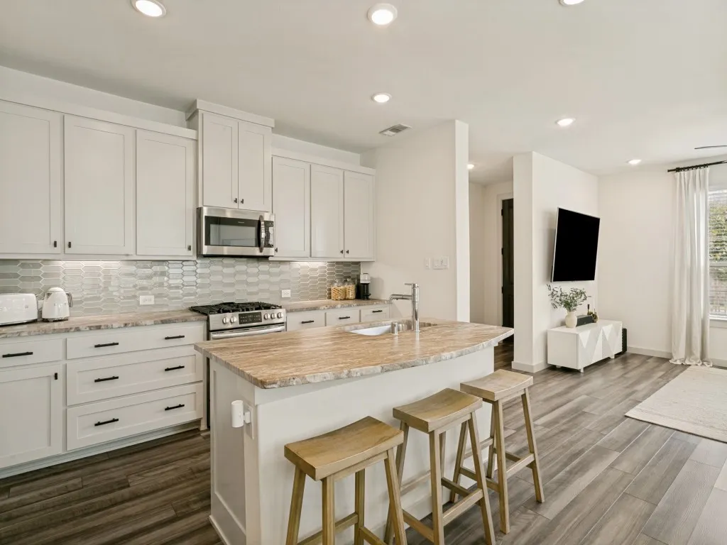 Kitchen featuring white shaker cabinets, stainless steel appliances, a patterned tile backsplash, and wood-finish flooring