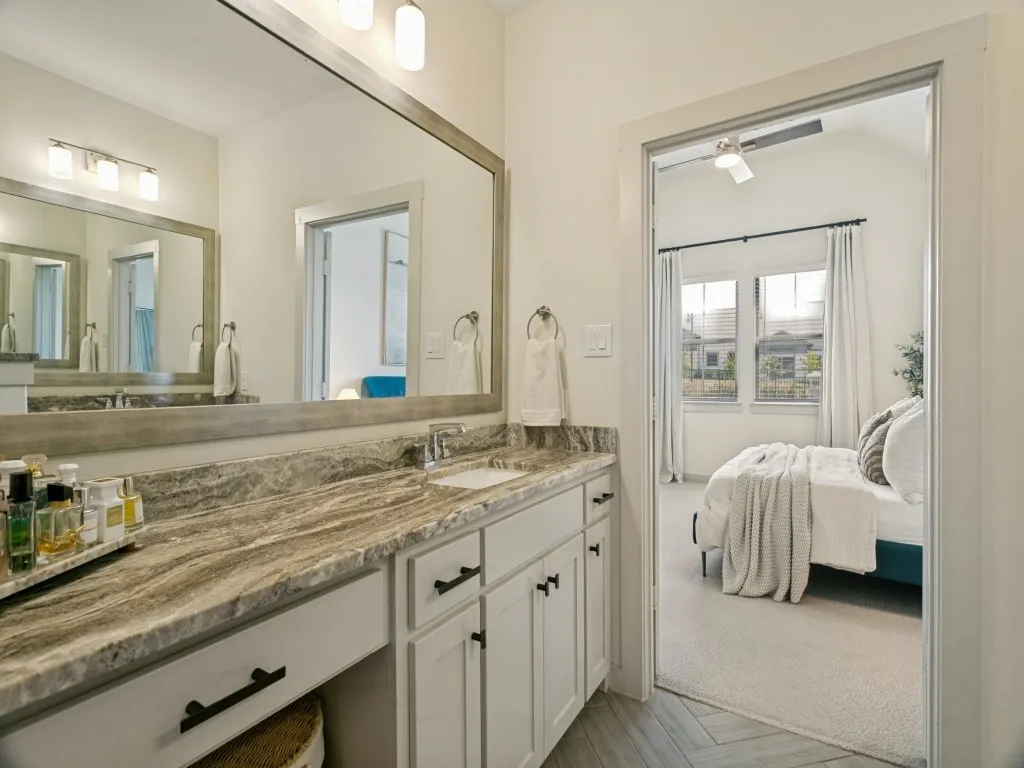 Dual vanity with a large framed mirror, stone countertop, undermount sink, and white cabinetry