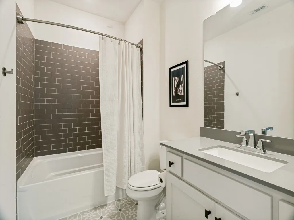 Bathroom featuring a tub and shower combination with gray subway tile surround, a single vanity with a light countertop, and patterned floor tile