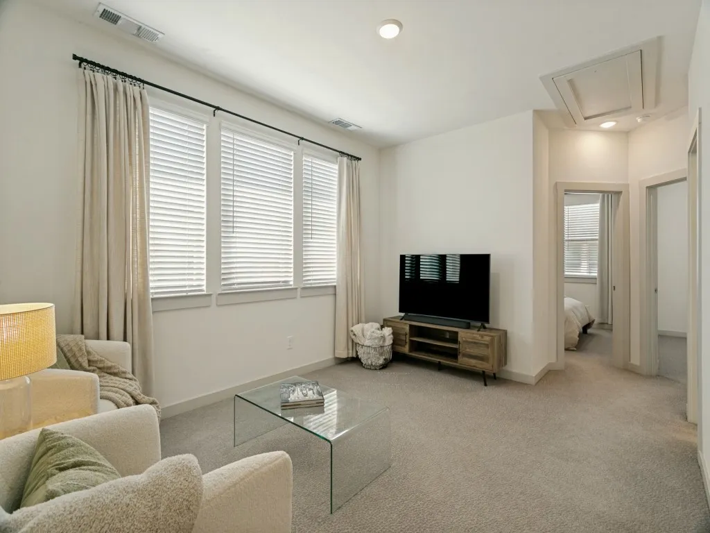 Light-toned wall finishes throughout, neutral carpeting, recessed ceiling lighting, three paneled windows, and a doorway leading to an additional room
