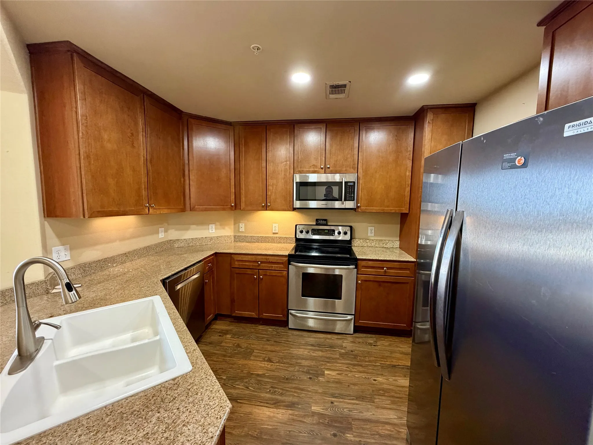 Kitchen featuring wood-finish cabinetry, stone-look countertops, a stainless steel appliance package, and wood-finish flooring