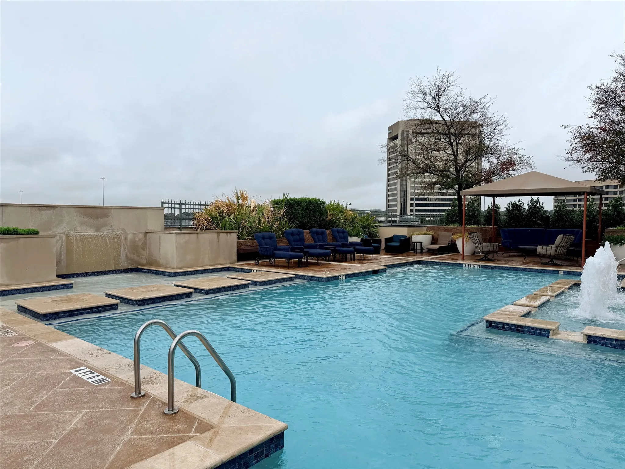 Expansive pool area featuring a built-in waterfall, integrated fountain, tiled steps, and a shaded cabana structure