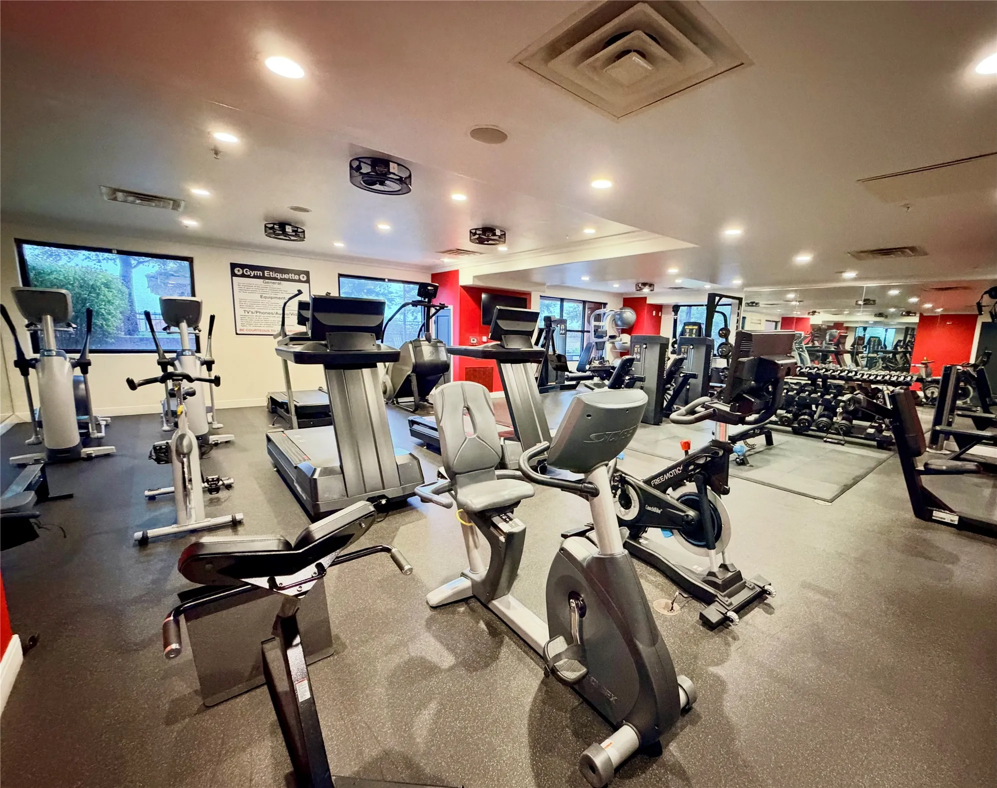 Spacious fitness center featuring a rubberized floor, mirrored wall, recessed lighting, and large windows