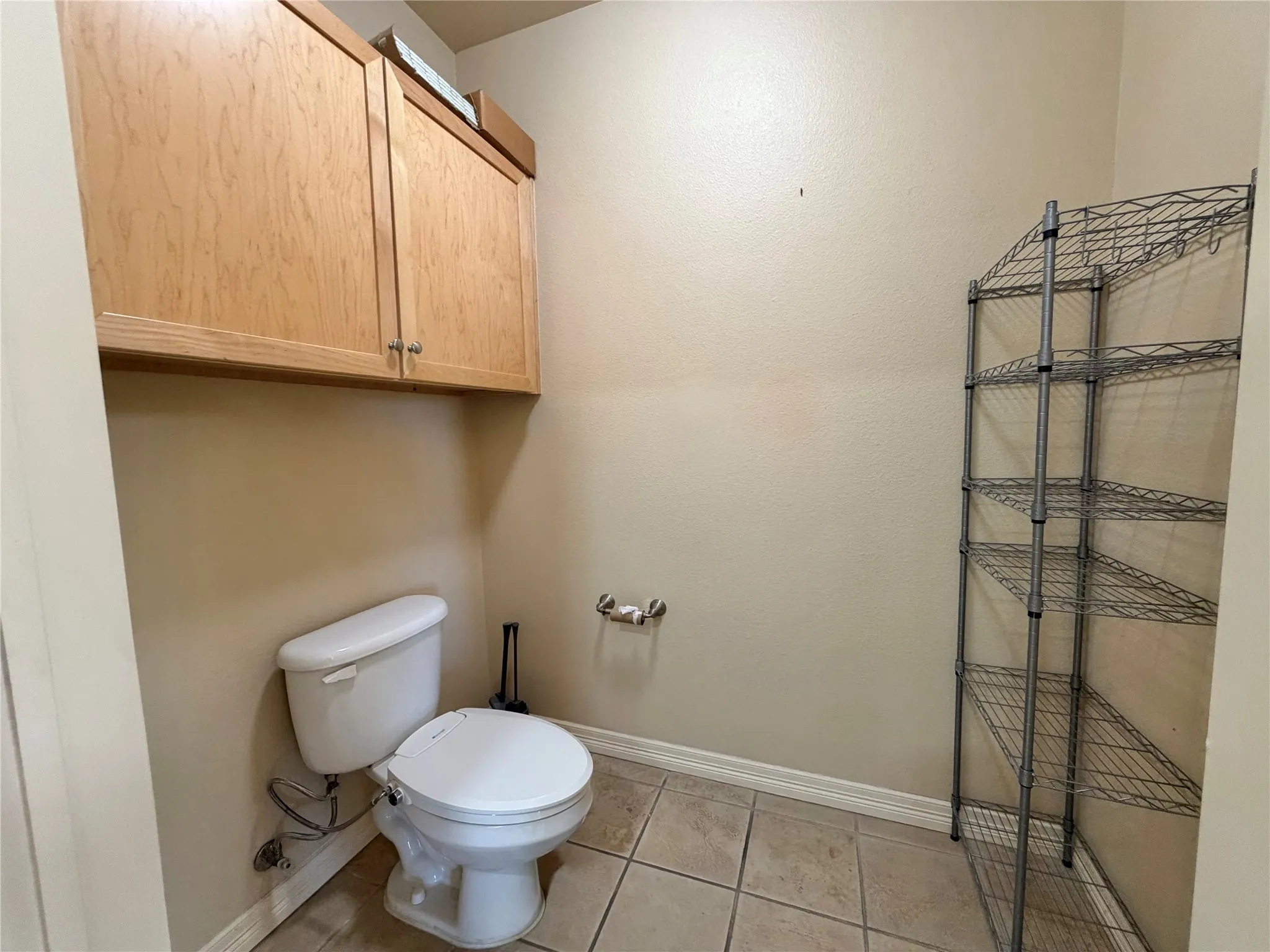 Overhead cabinetry with wood-finish doors and metal pulls, alongside a white toilet, and tiled flooring