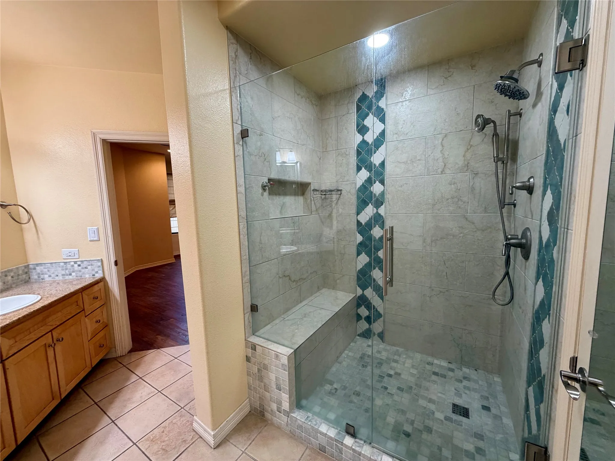 Glass-enclosed shower with a built-in bench, dual shower heads, and decorative tile accents